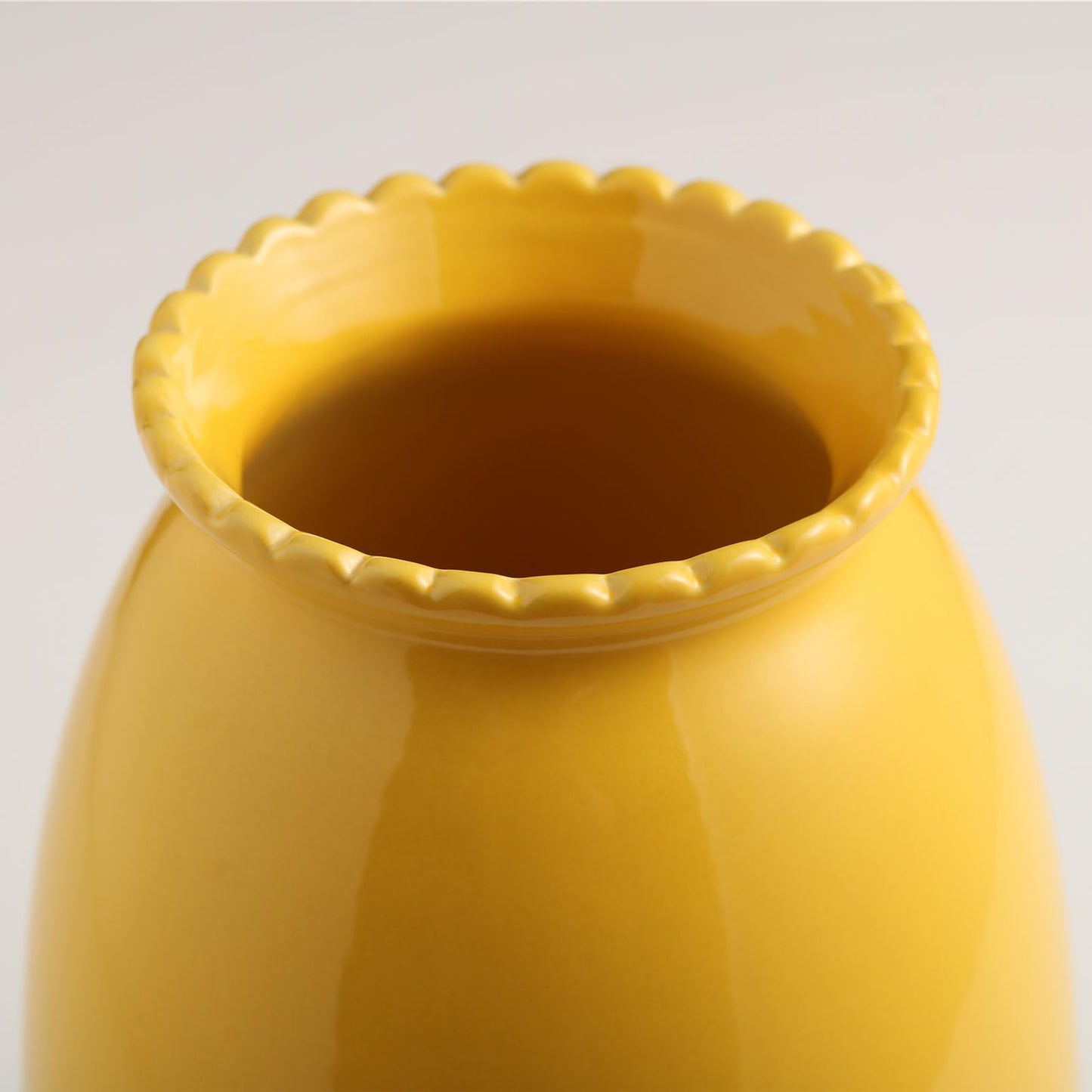 Yellow ceramic vase with scalloped rim on a light gray background