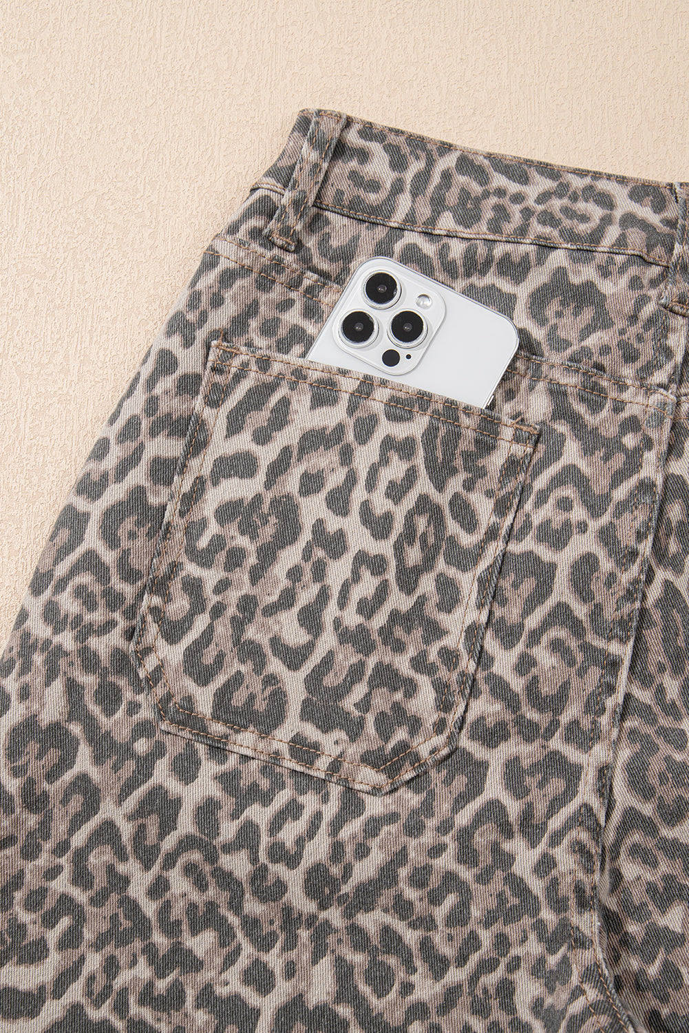 Leopard print pants with a phone case in the pocket on a beige background