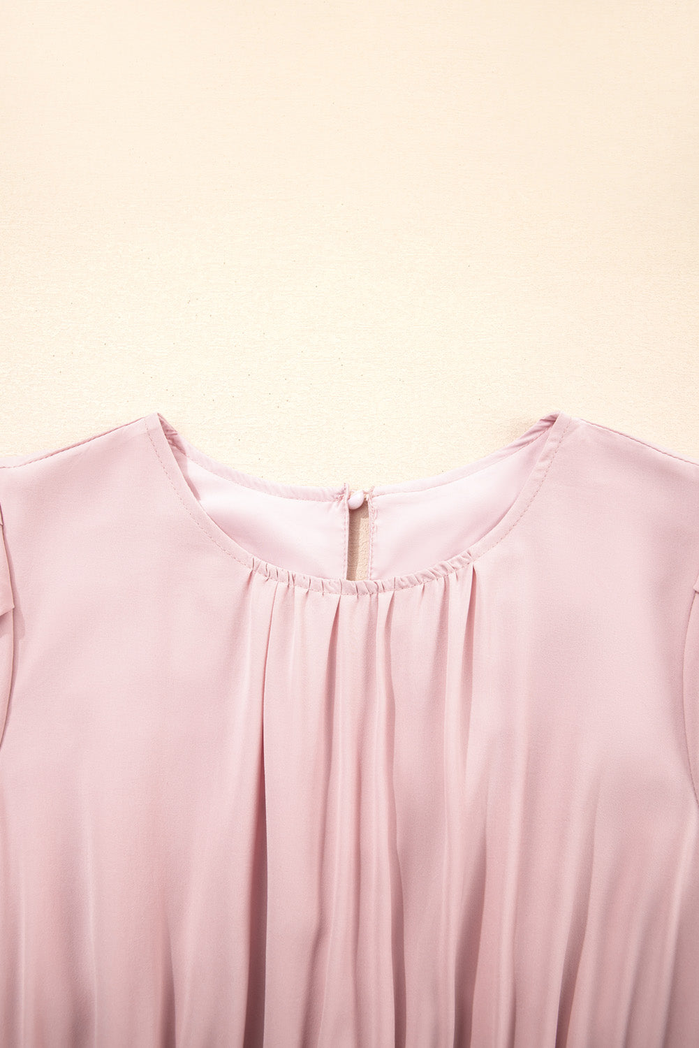 Close-up of a light pink sleeveless top on a beige background