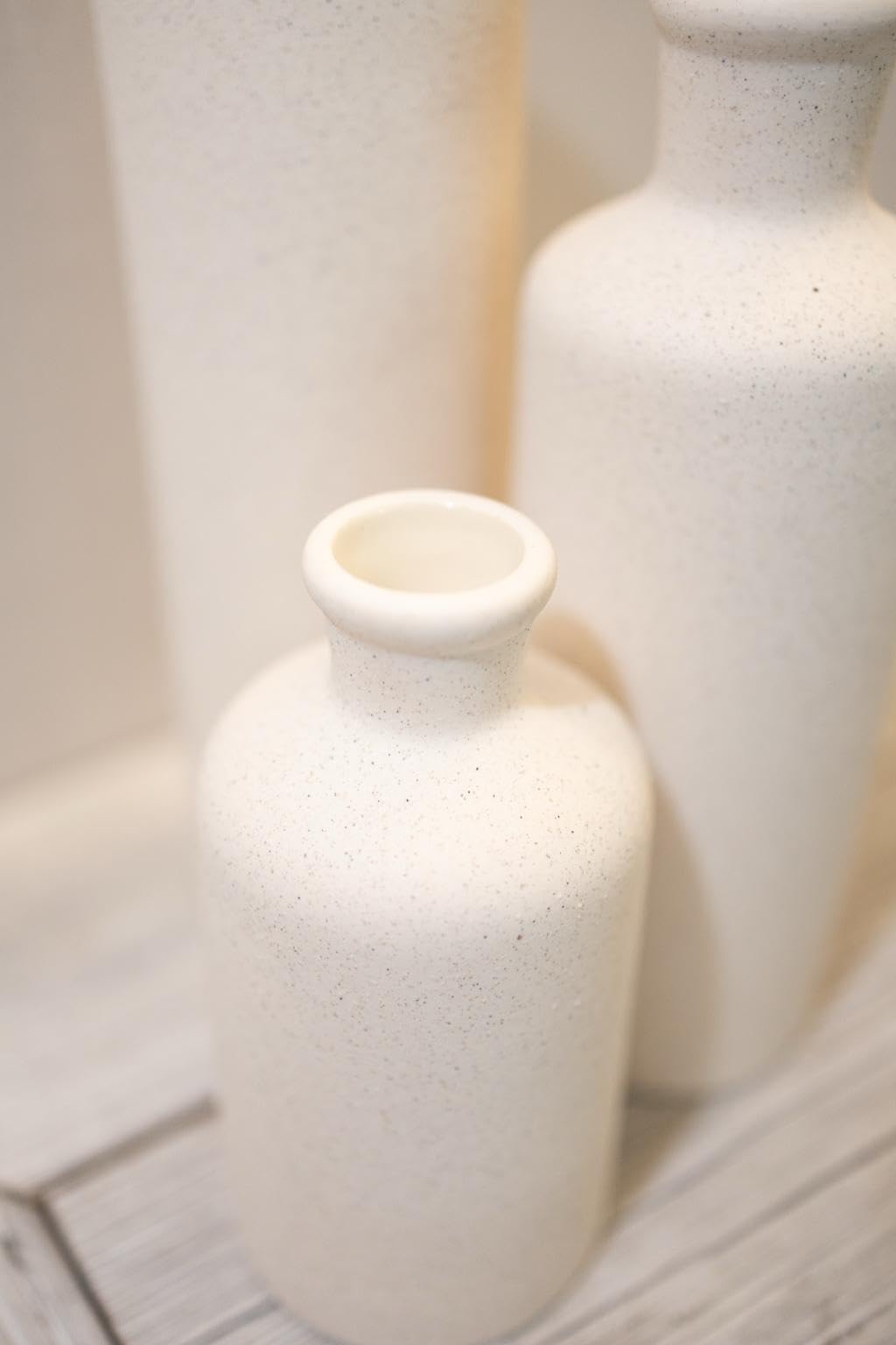Two white ceramic vases on a textured surface with a blurred background