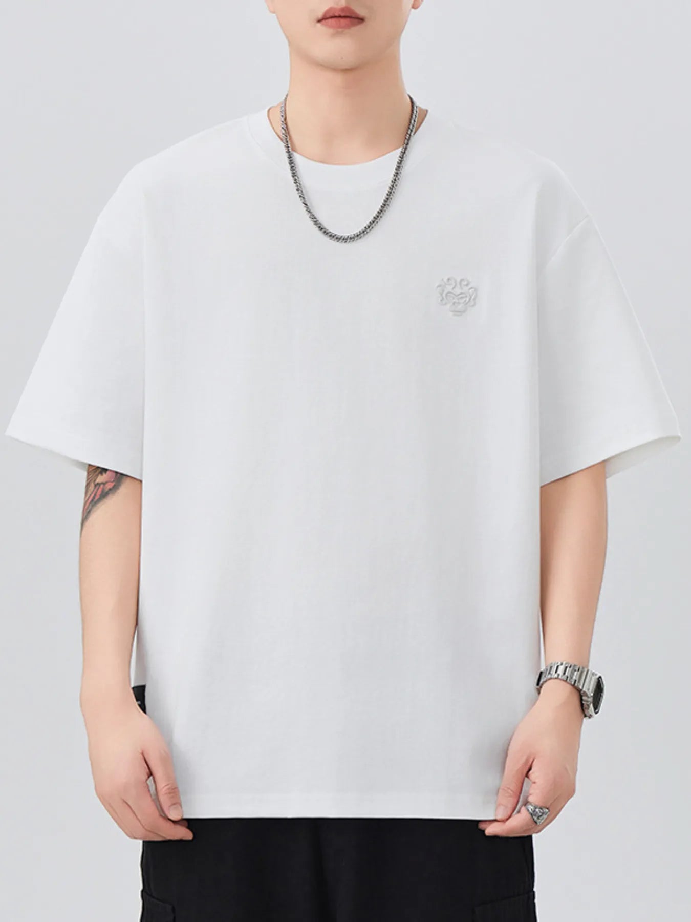 Person wearing a plain white t-shirt with a small logo on a light gray background