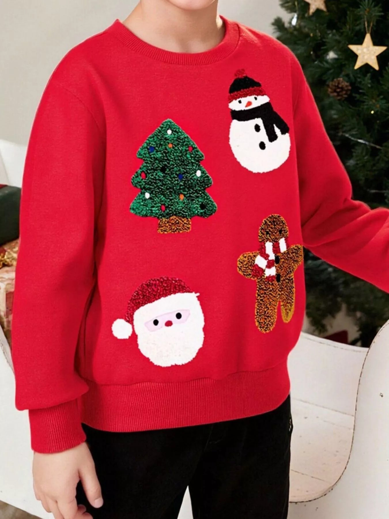 Child wearing a red Christmas sweater with festive designs in a decorated room.