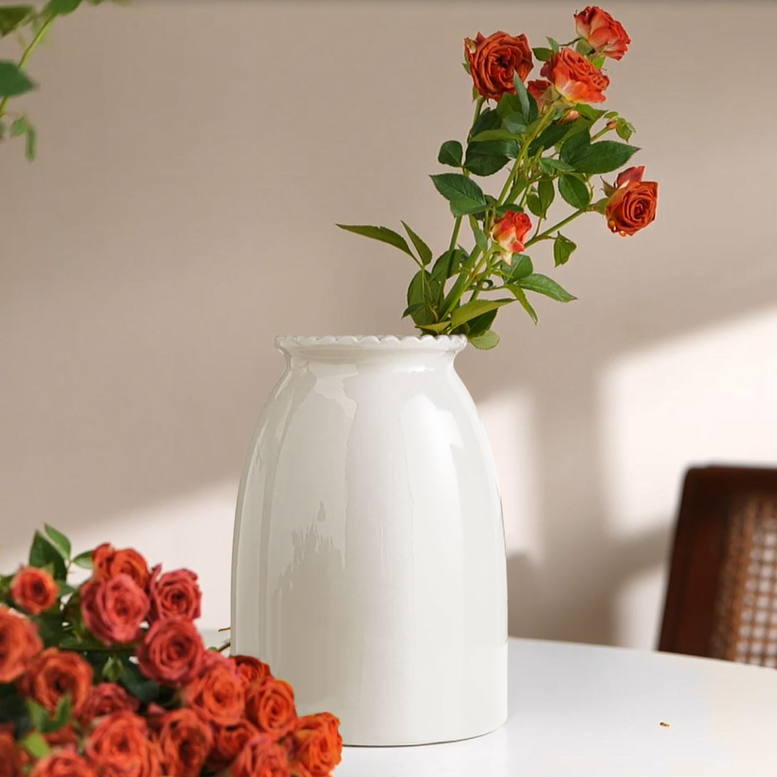 White vase with red roses on a table against a neutral wall