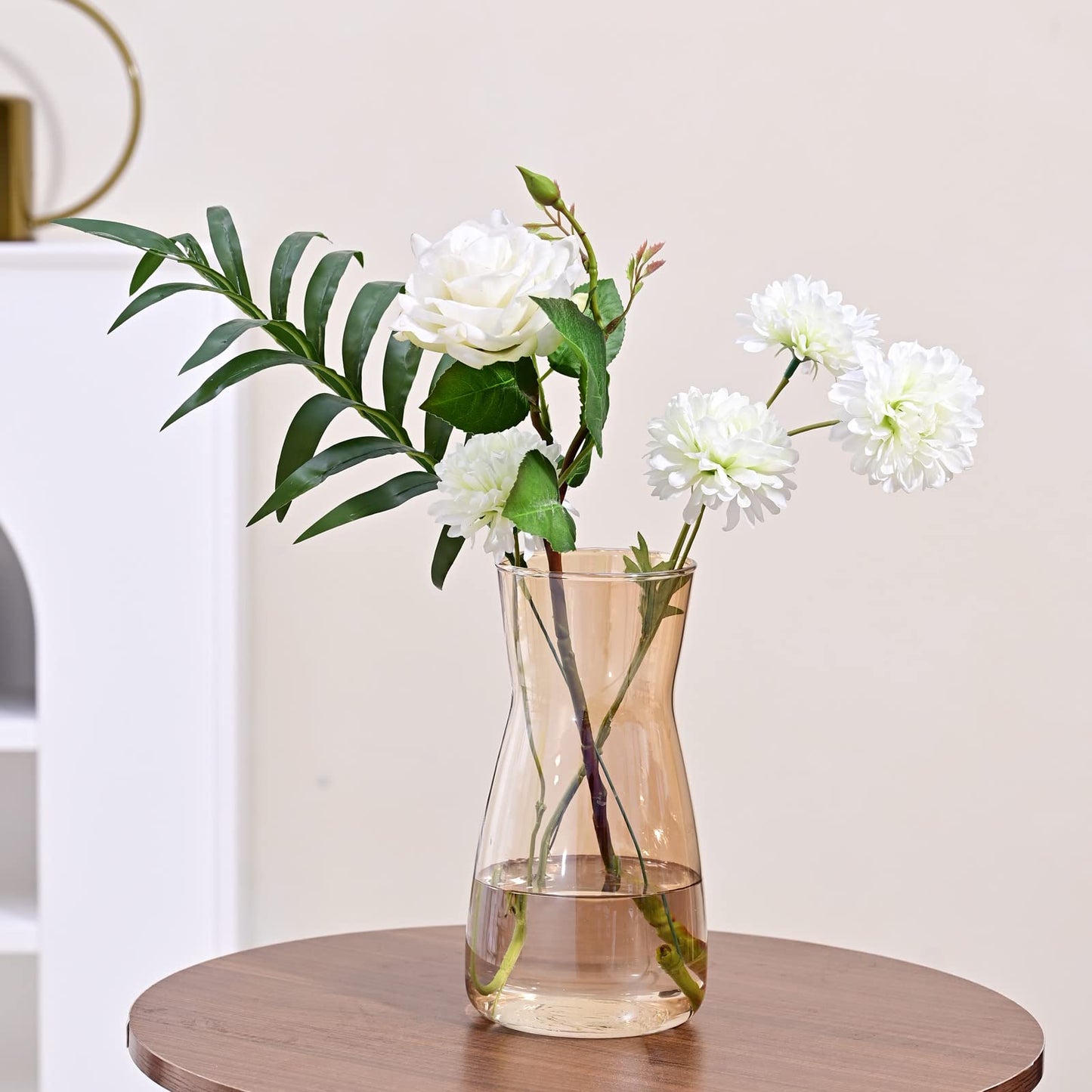 Clear vase with white flowers and green leaves on a wooden table