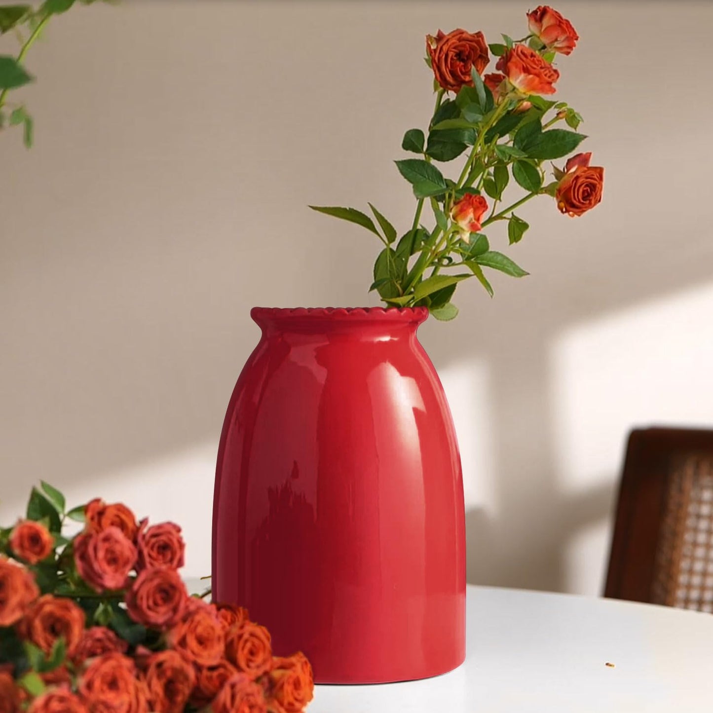 Red vase with orange roses on a table against a neutral background