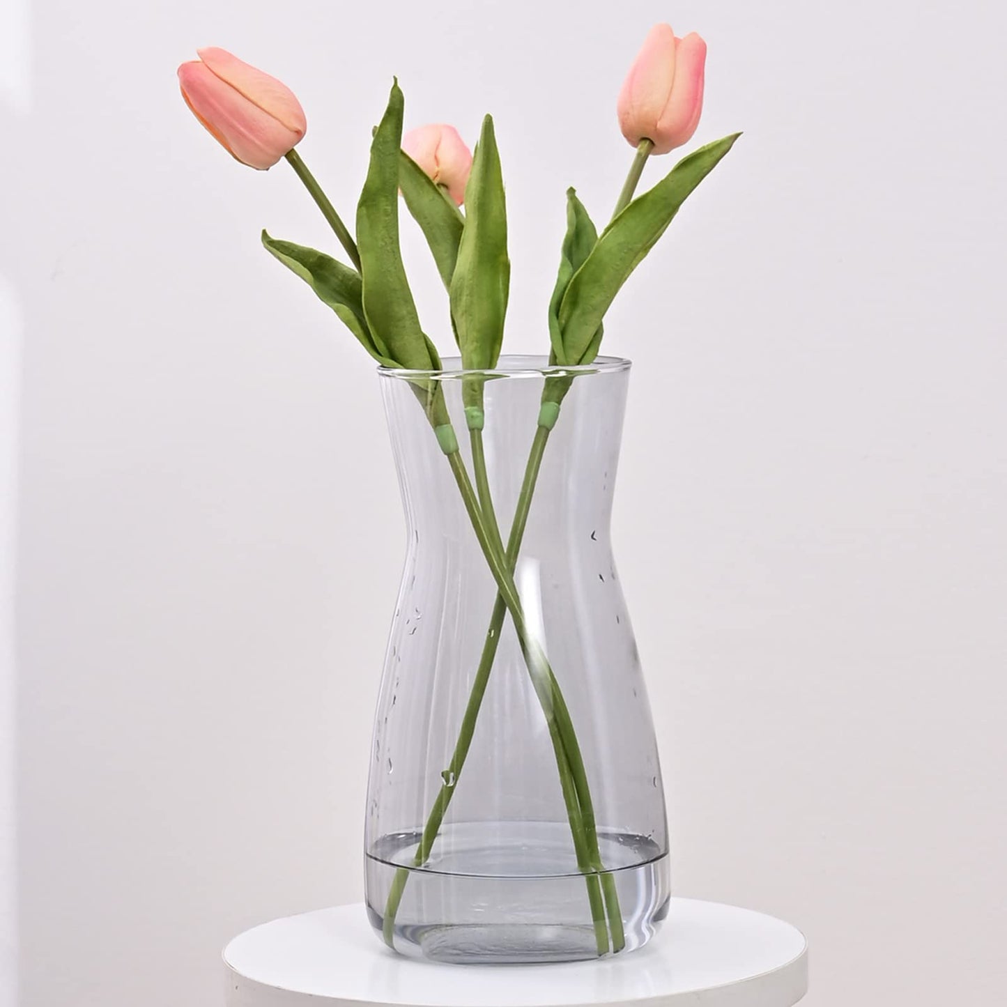 Clear glass vase with pink tulips on a white surface and light gray background