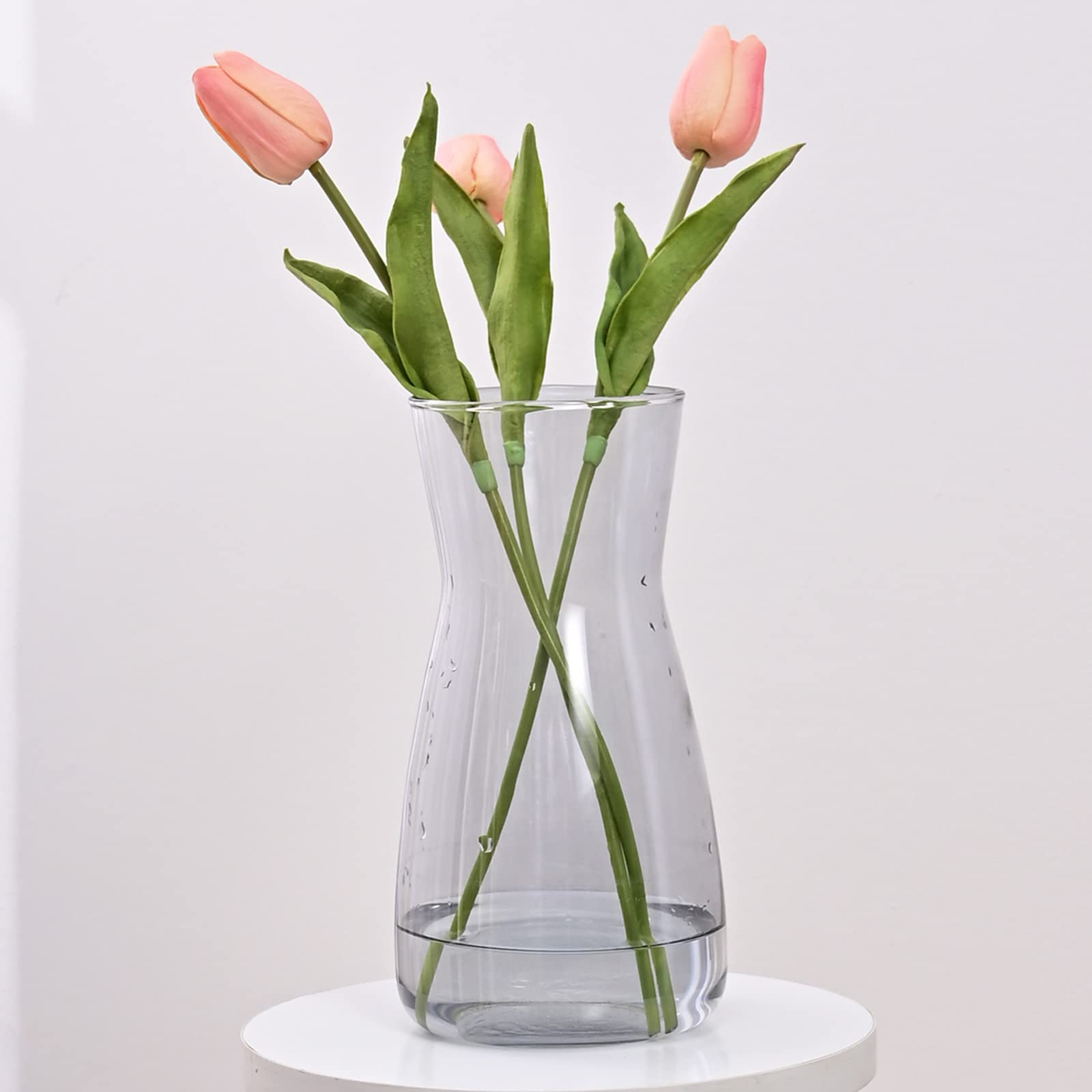 Clear glass vase with pink tulips on a white surface and light gray background