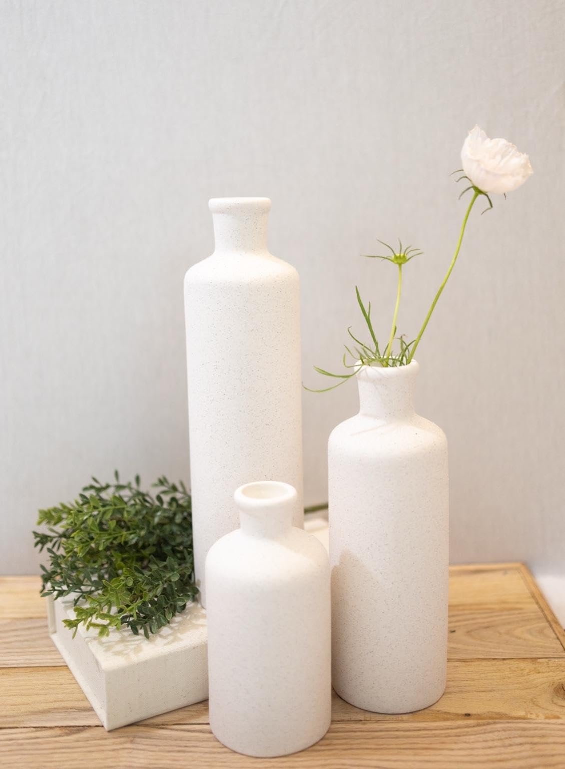 Three white ceramic vases on a wooden surface with a light gray background