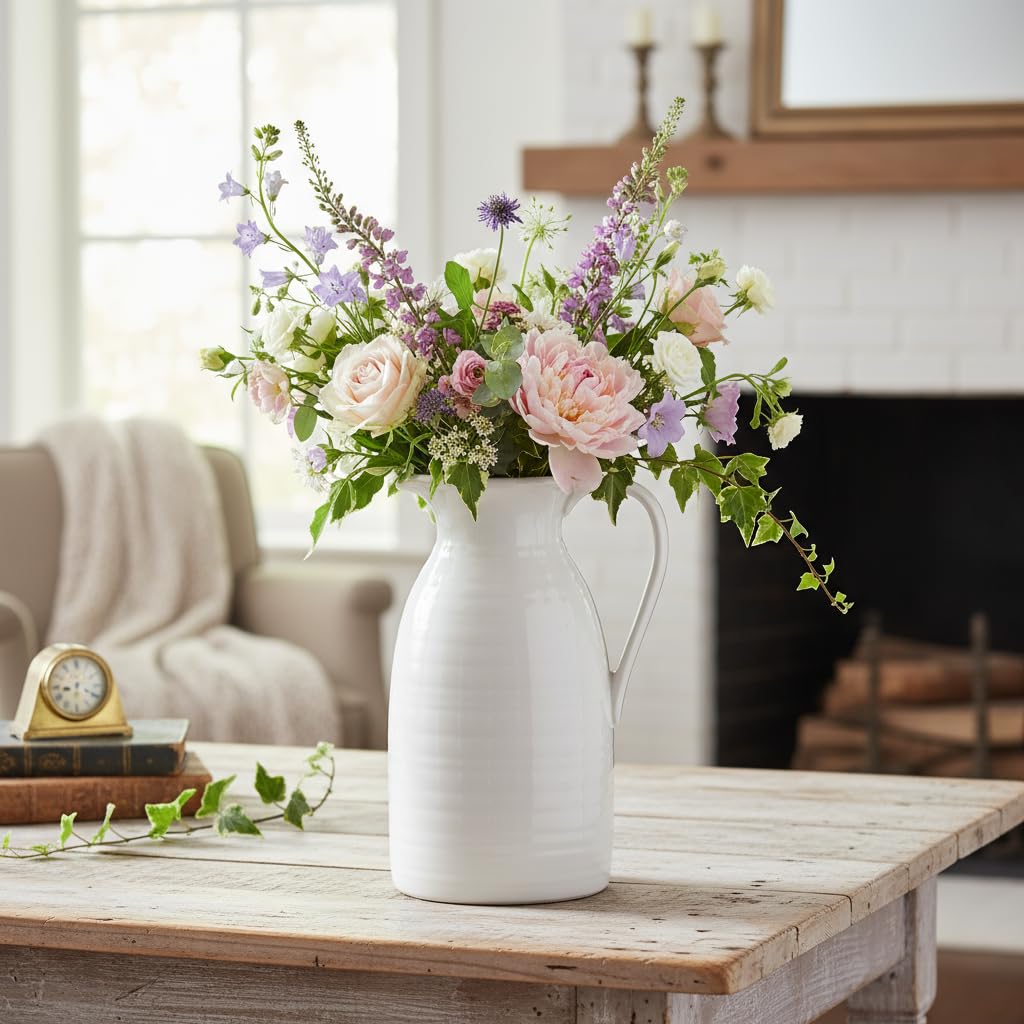 White vase with pink and purple flowers on a wooden table in a living room.