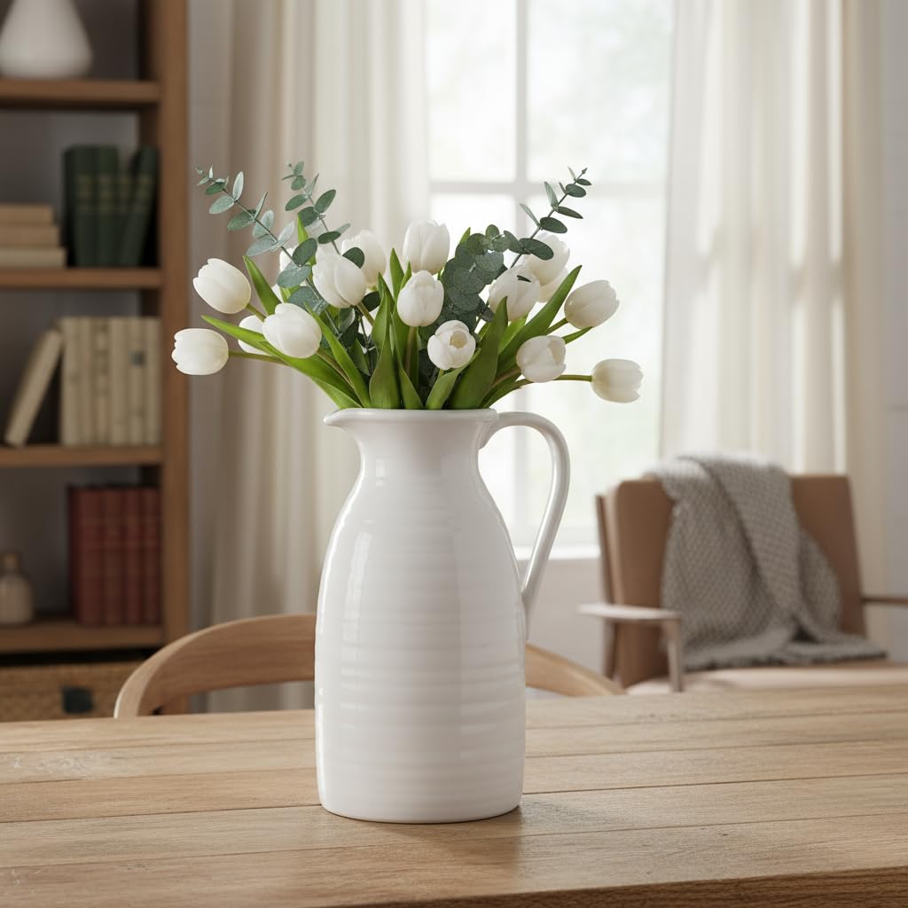 White vase with artificial tulips on a wooden table in a room with books and a chair.