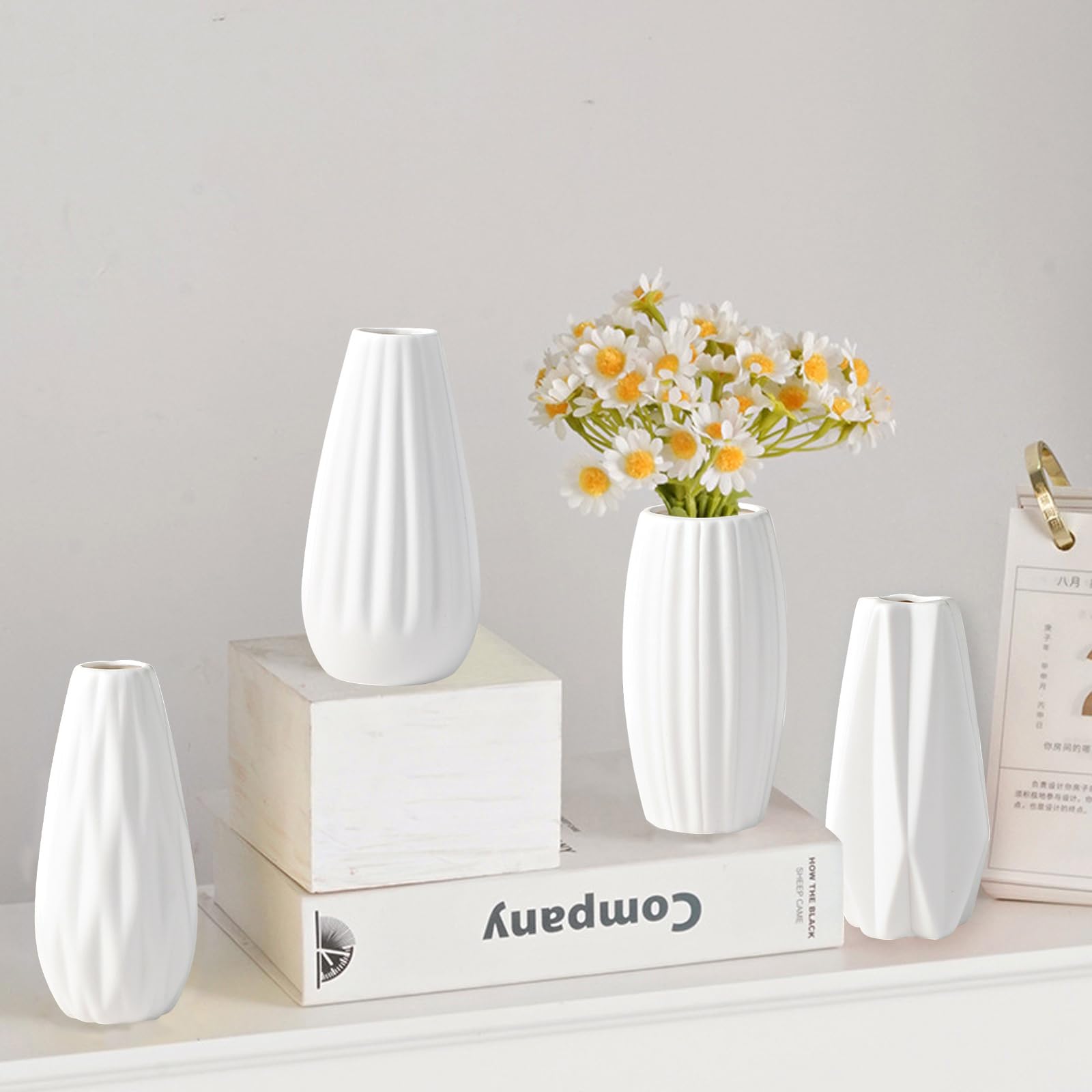 Set of white ceramic vases on a shelf with a small bouquet of flowers.