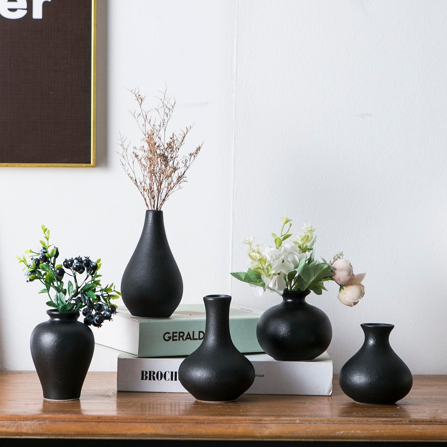 Set of black vases on a wooden surface with books and decorative plants.