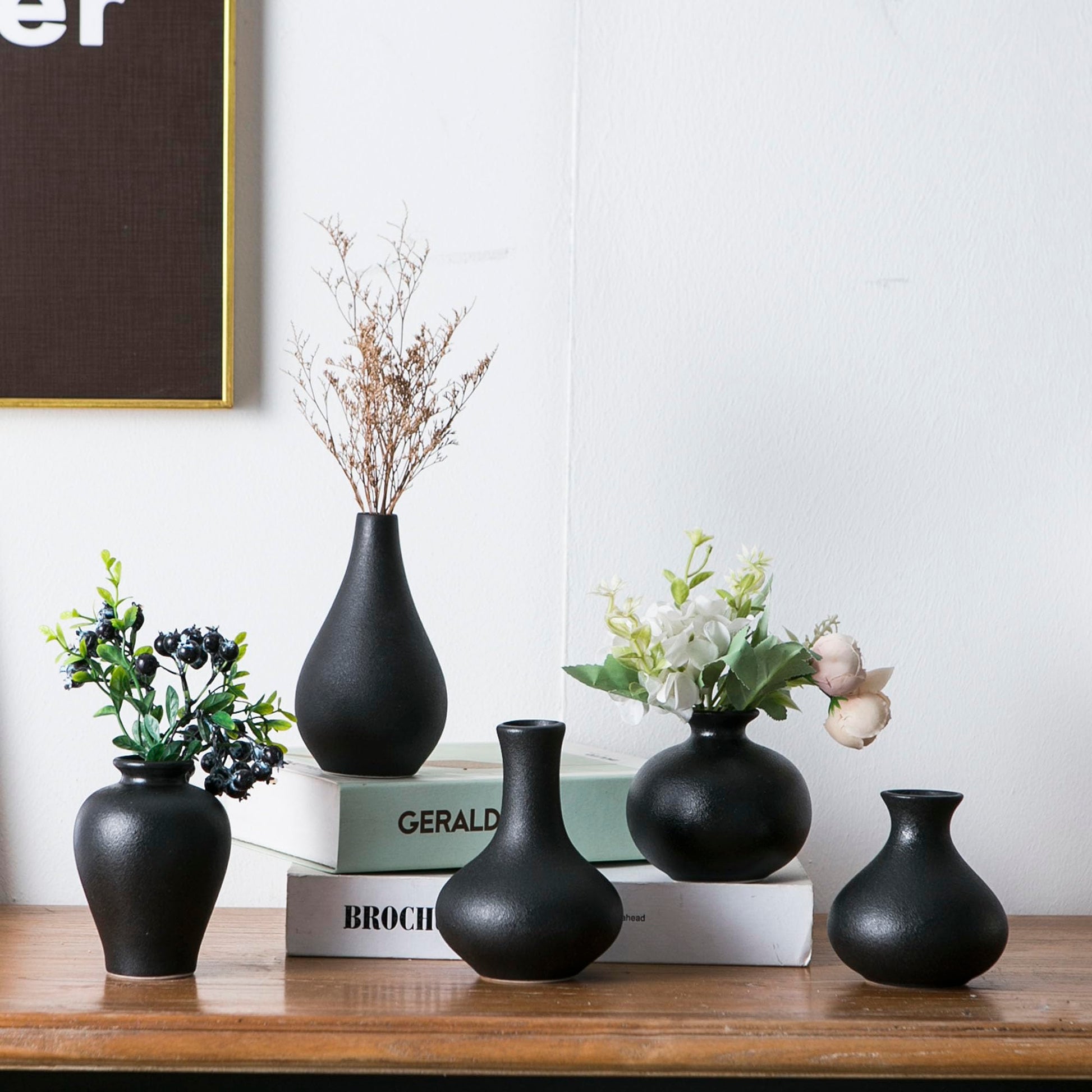 Set of black vases on a wooden surface with books and decorative plants.