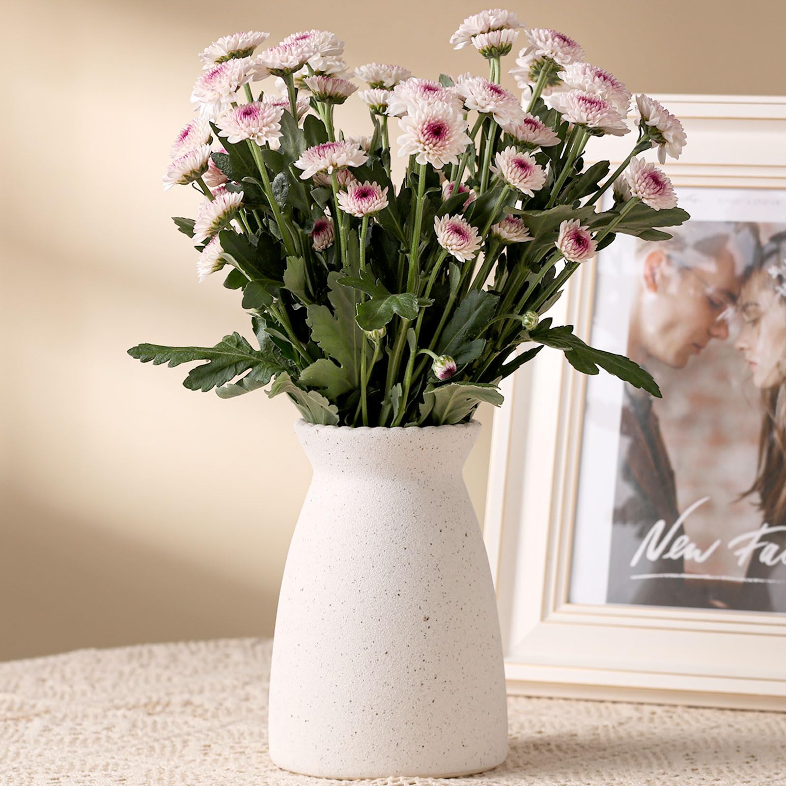 White vase with pink flowers on a surface with a blurred background