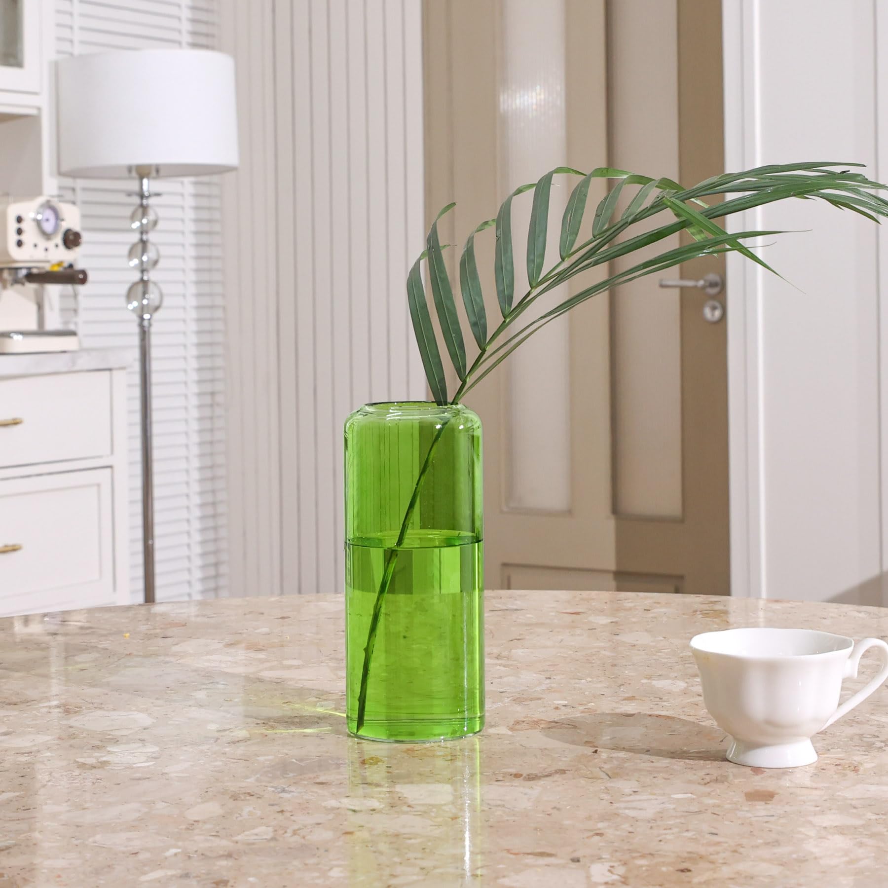 Green glass vase with a leaf on a marble surface in a kitchen setting