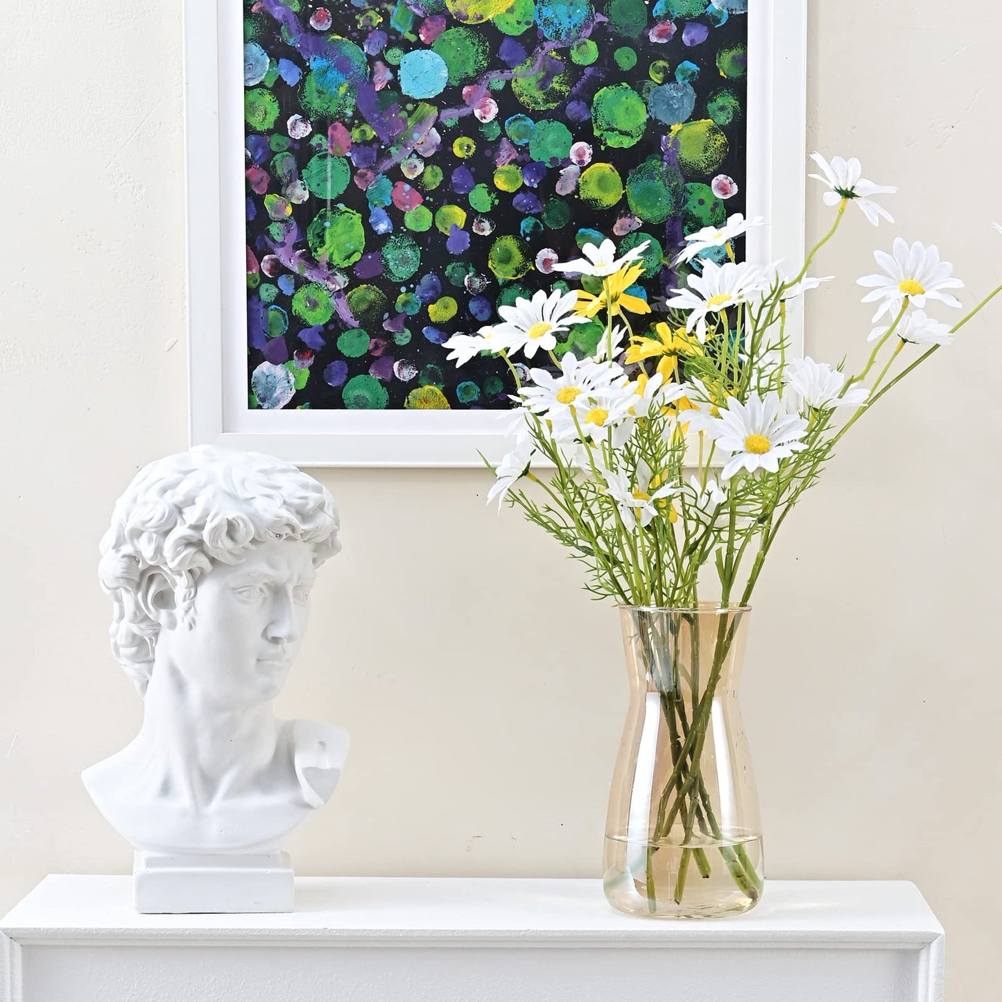 Vase of flowers on a white surface with a classical bust and abstract painting in the background.