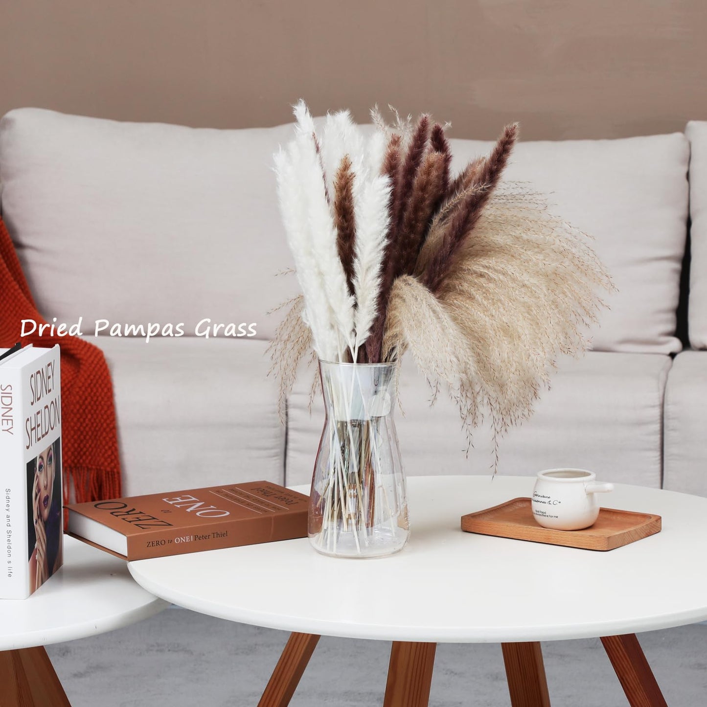 Dried pampas grass in a vase on a coffee table with books and a mug in a living room setting.