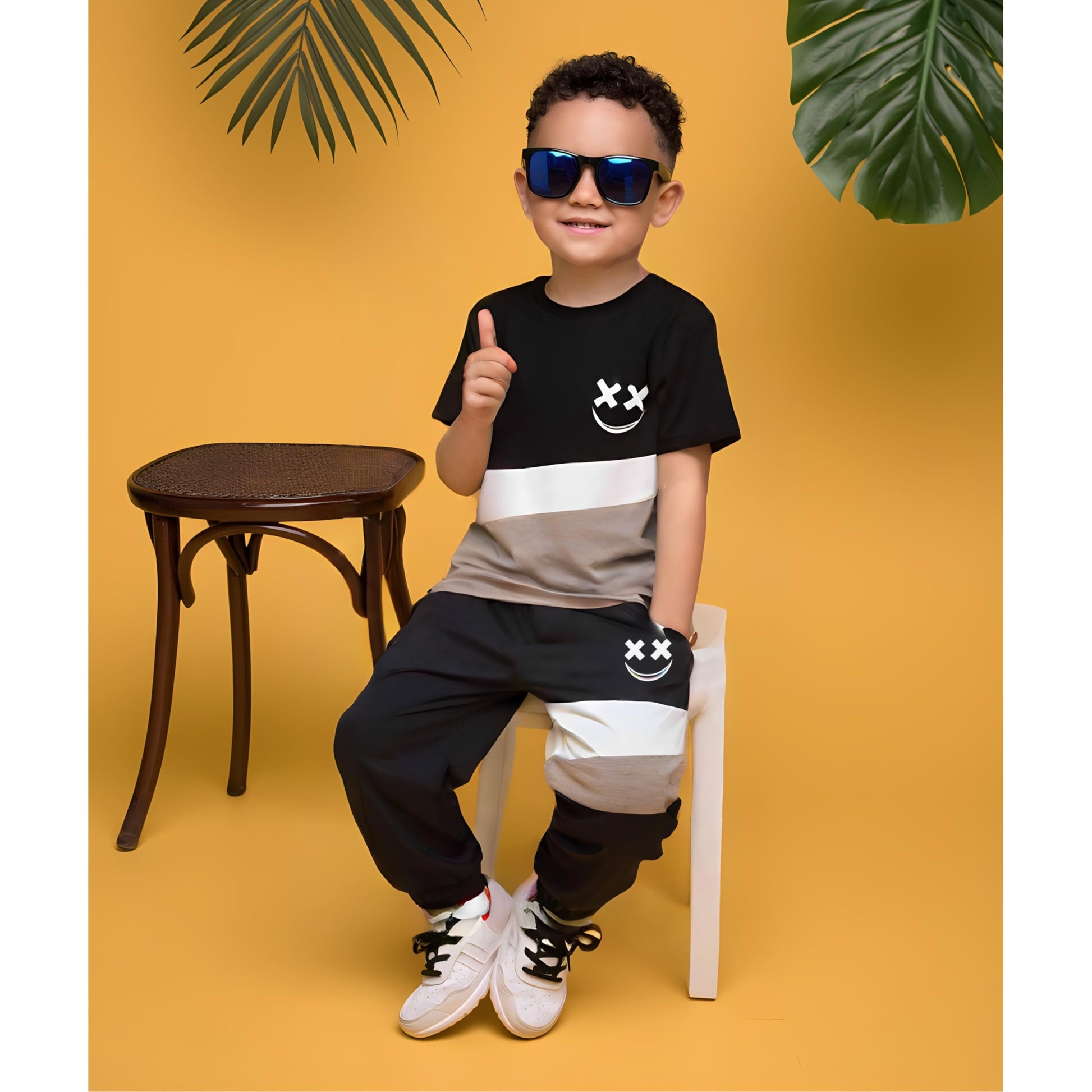 Child wearing a black and white striped shirt with a smiley face design, sitting on a stool against a yellow background.