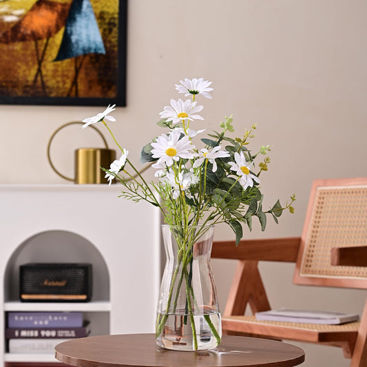 Clear glass vase with daisies on a wooden table in a room setting.