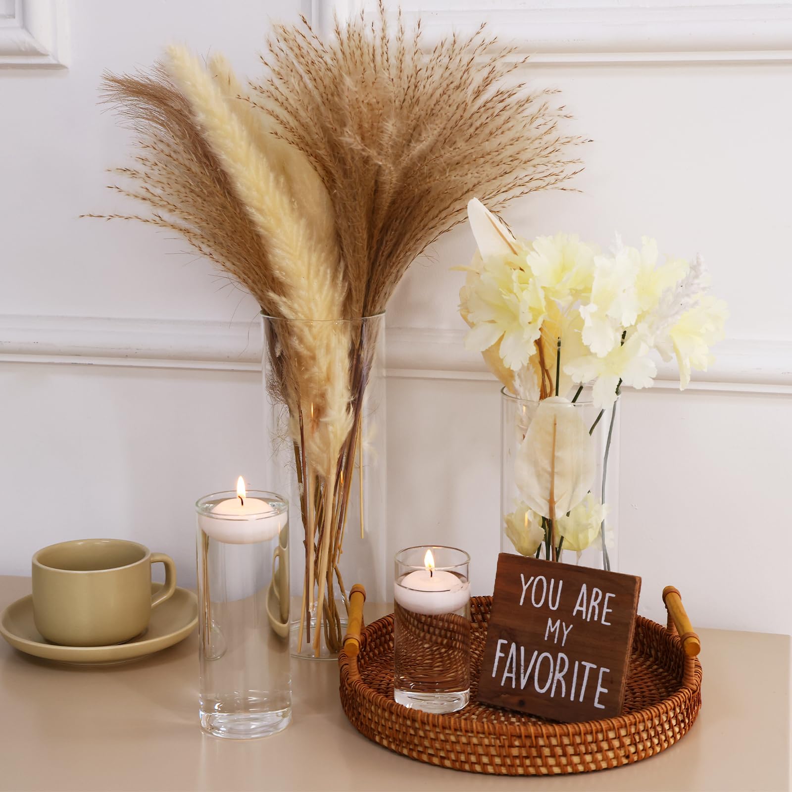 Decorative setup with pampas grass, candles, flowers, and a sign on a table.