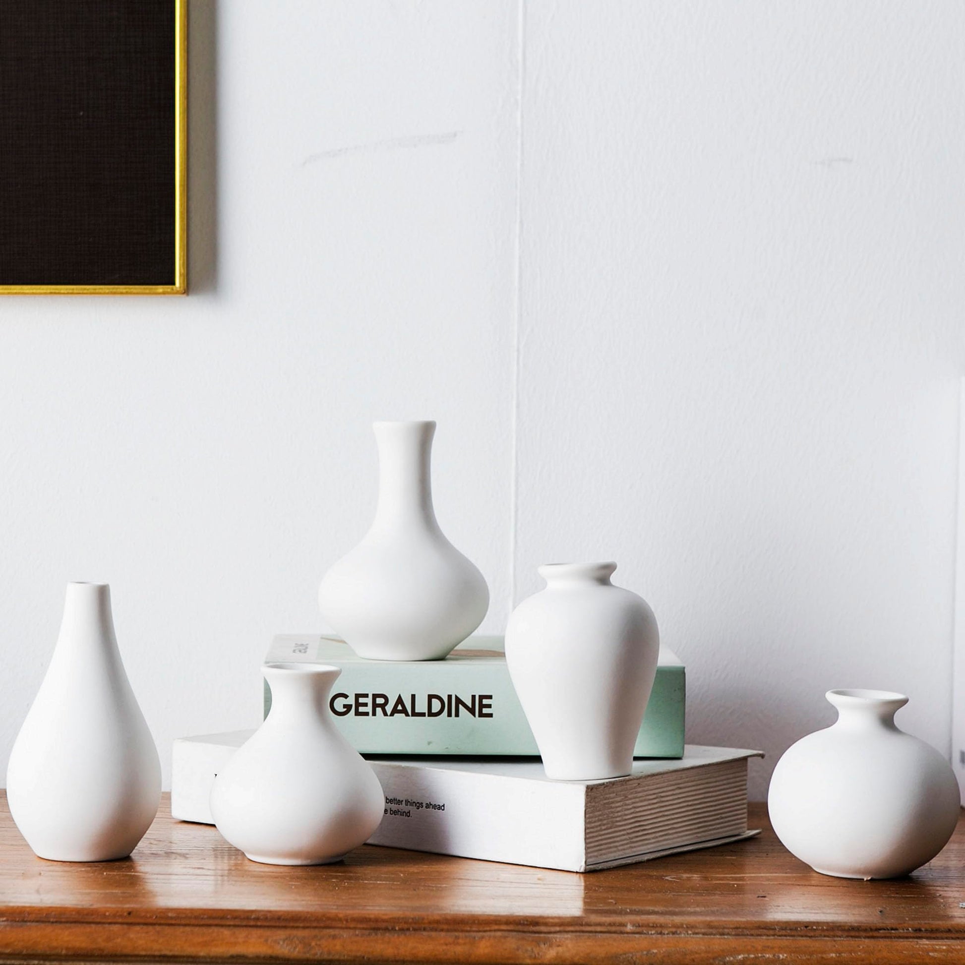 Set of white vases on a wooden surface with a book titled 'Geraldine' in the background.