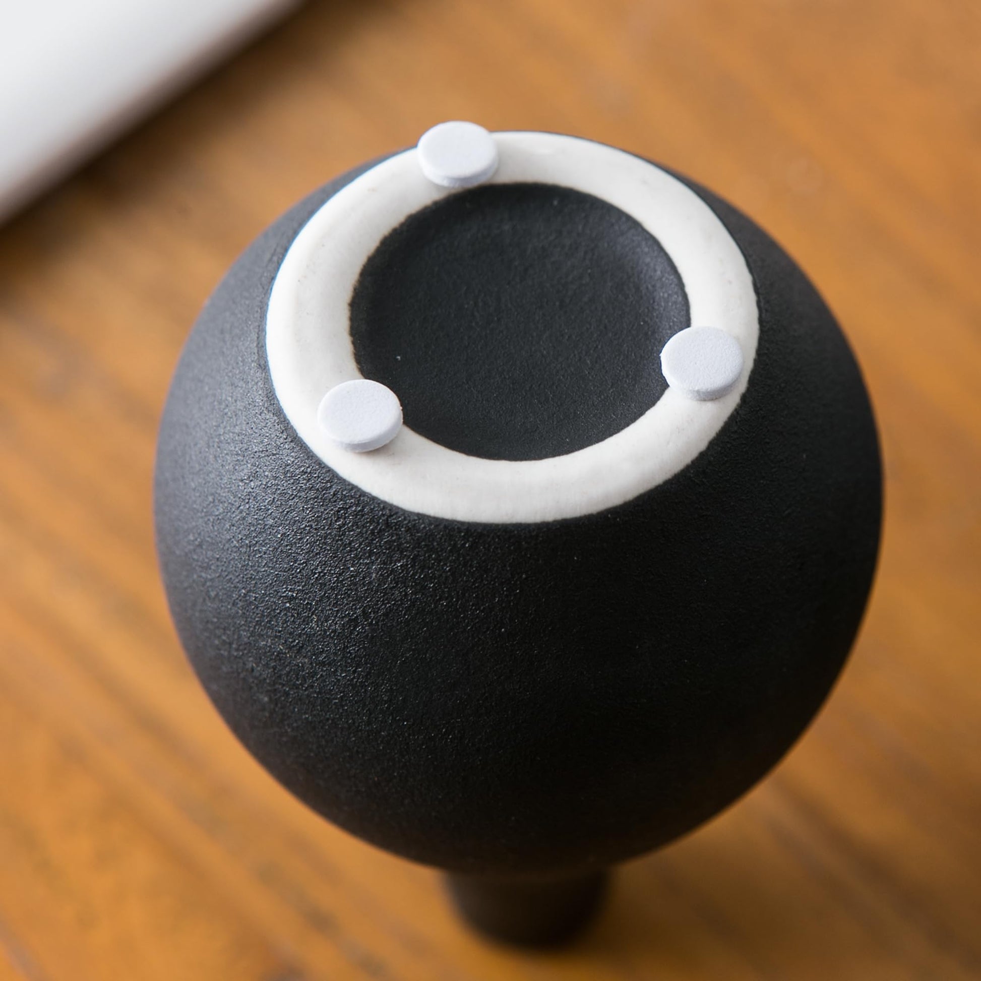 Black spherical object with a white circular ring and four gray knobs on a wooden surface