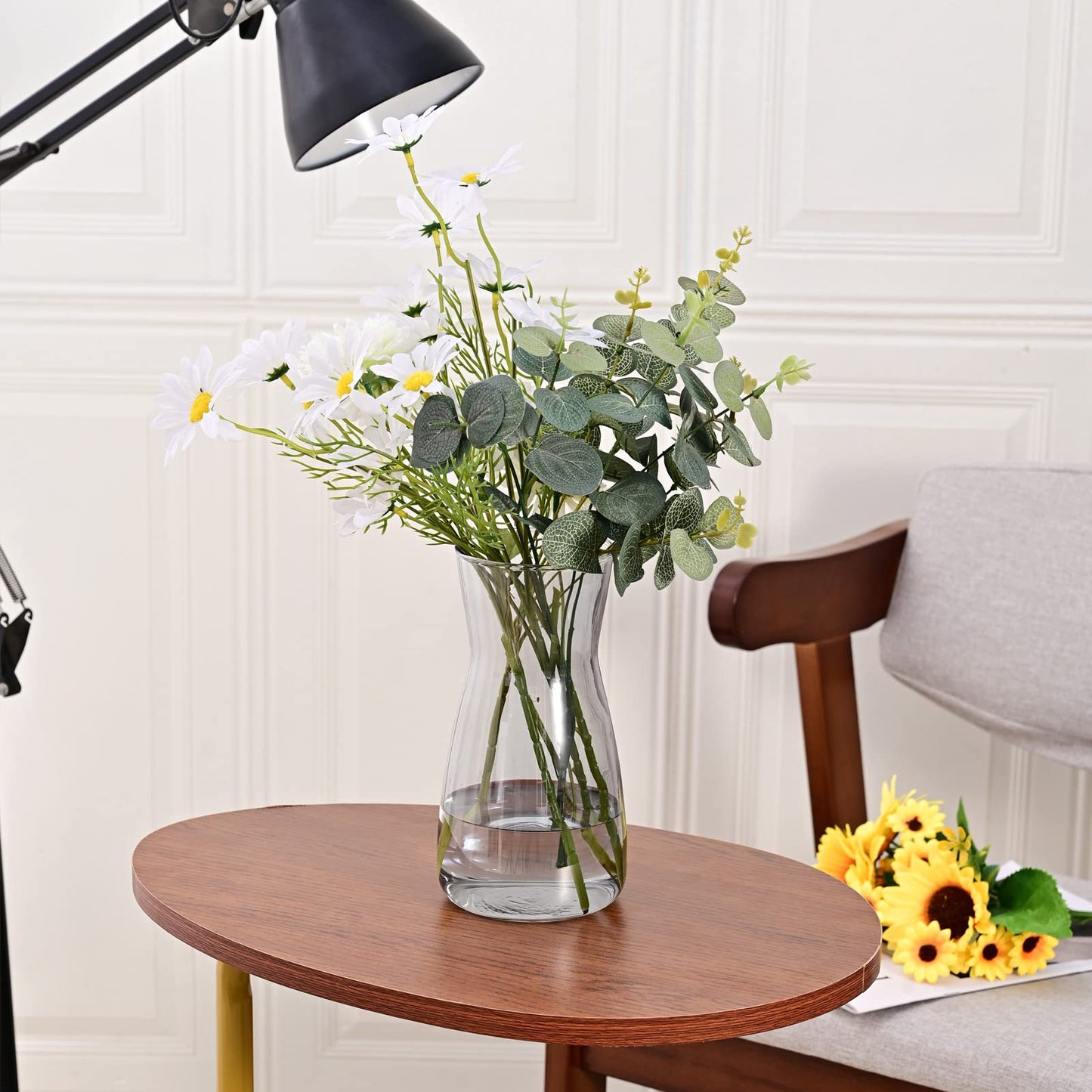 Clear vase with flowers on a wooden table, lamp and chair in the background