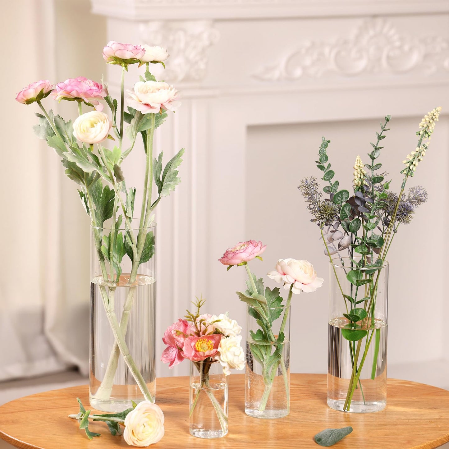 Set of floral arrangements in clear vases on a wooden table with a neutral background