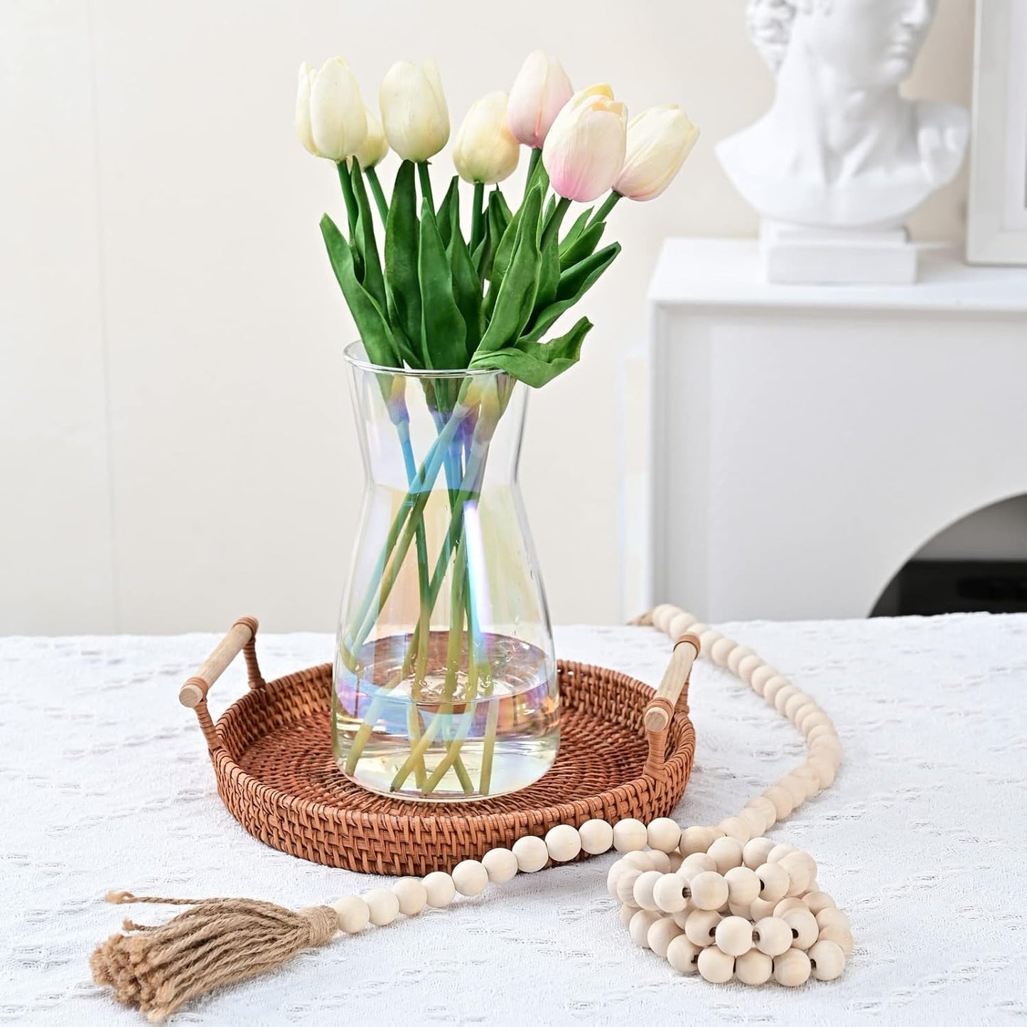 Clear vase with tulips on a woven tray on a white surface