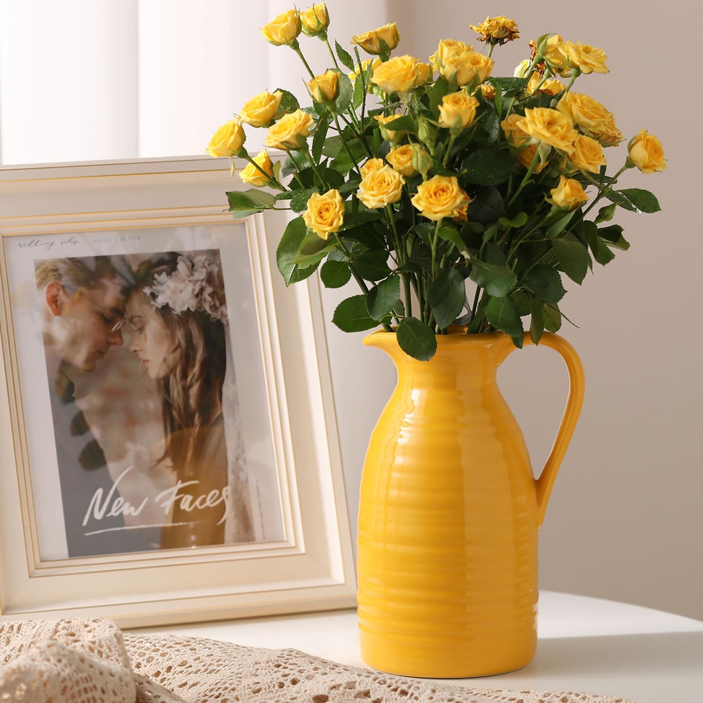 Yellow vase with flowers on a surface next to a framed photo