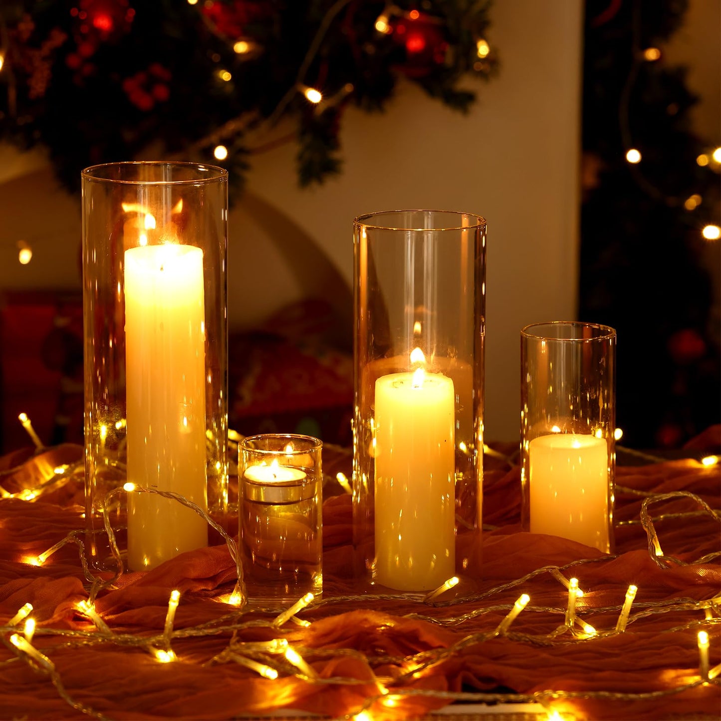 Candlelit scene with tall and short candles in glass holders on a wooden surface with string lights.
