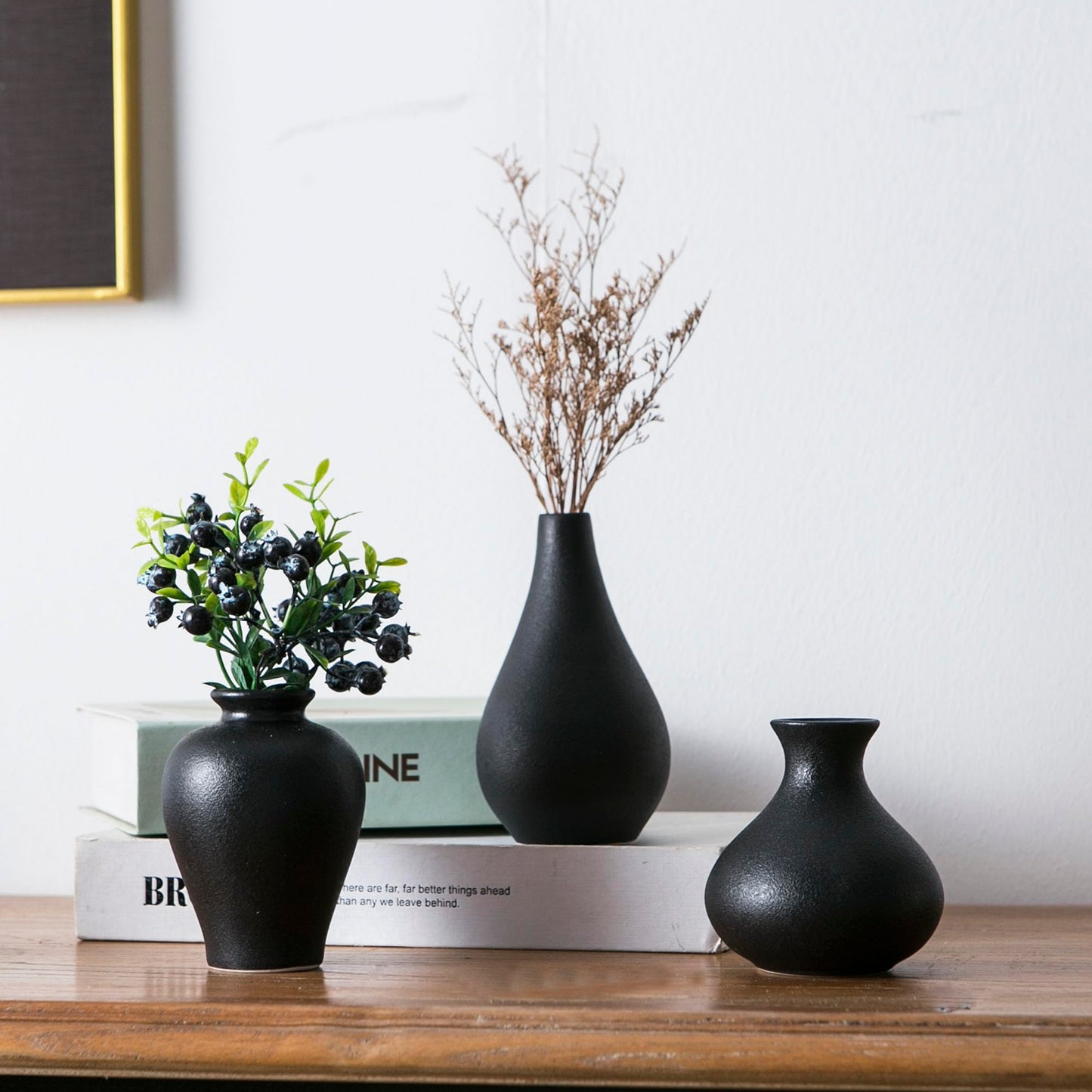 Three black vases on a wooden surface with a minimal background