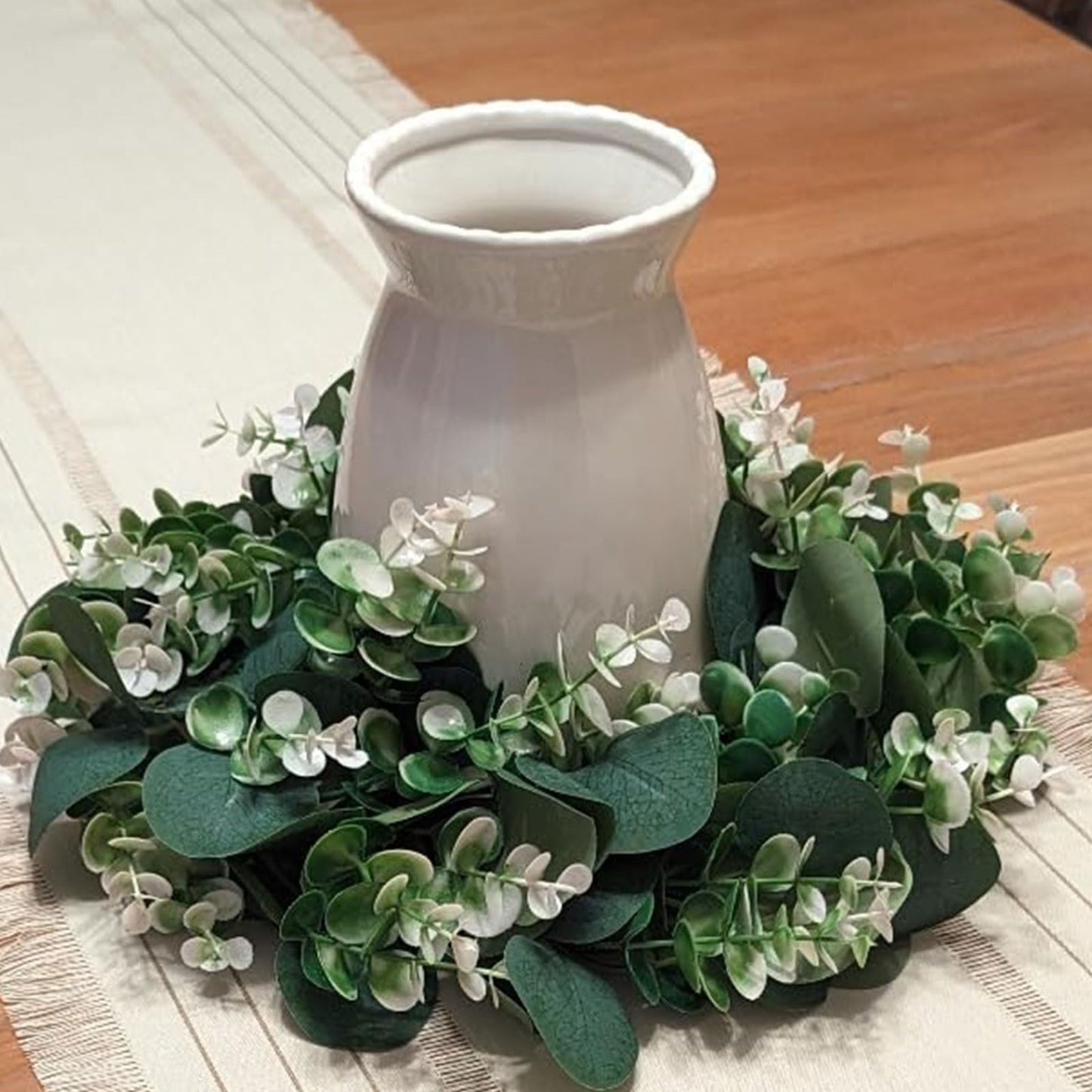 White vase surrounded by green foliage on a wooden surface