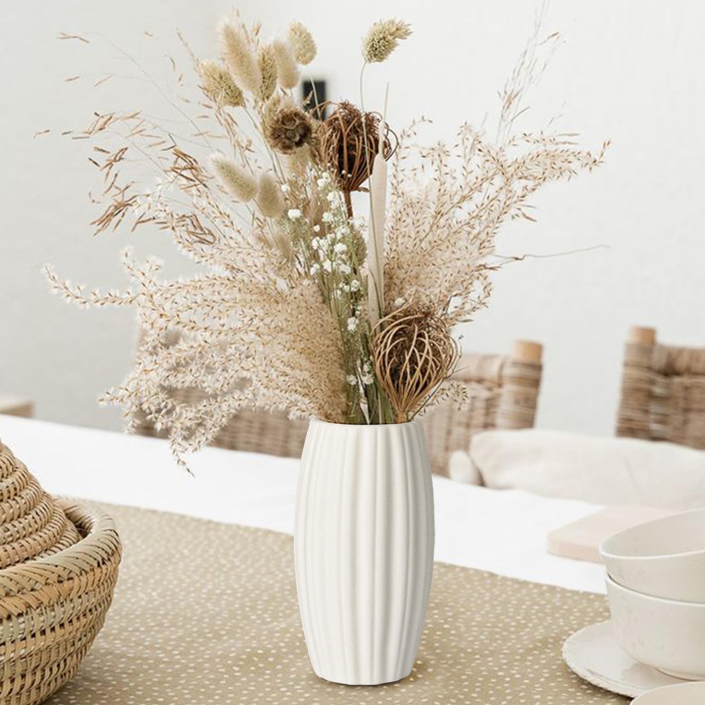 White vase with dried flowers on a table in a cozy room.