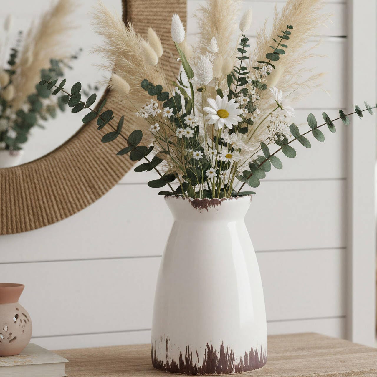 White vase with flowers on a wooden surface with a decorative wall in the background