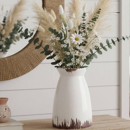 White vase with flowers on a wooden surface with a decorative wall in the background