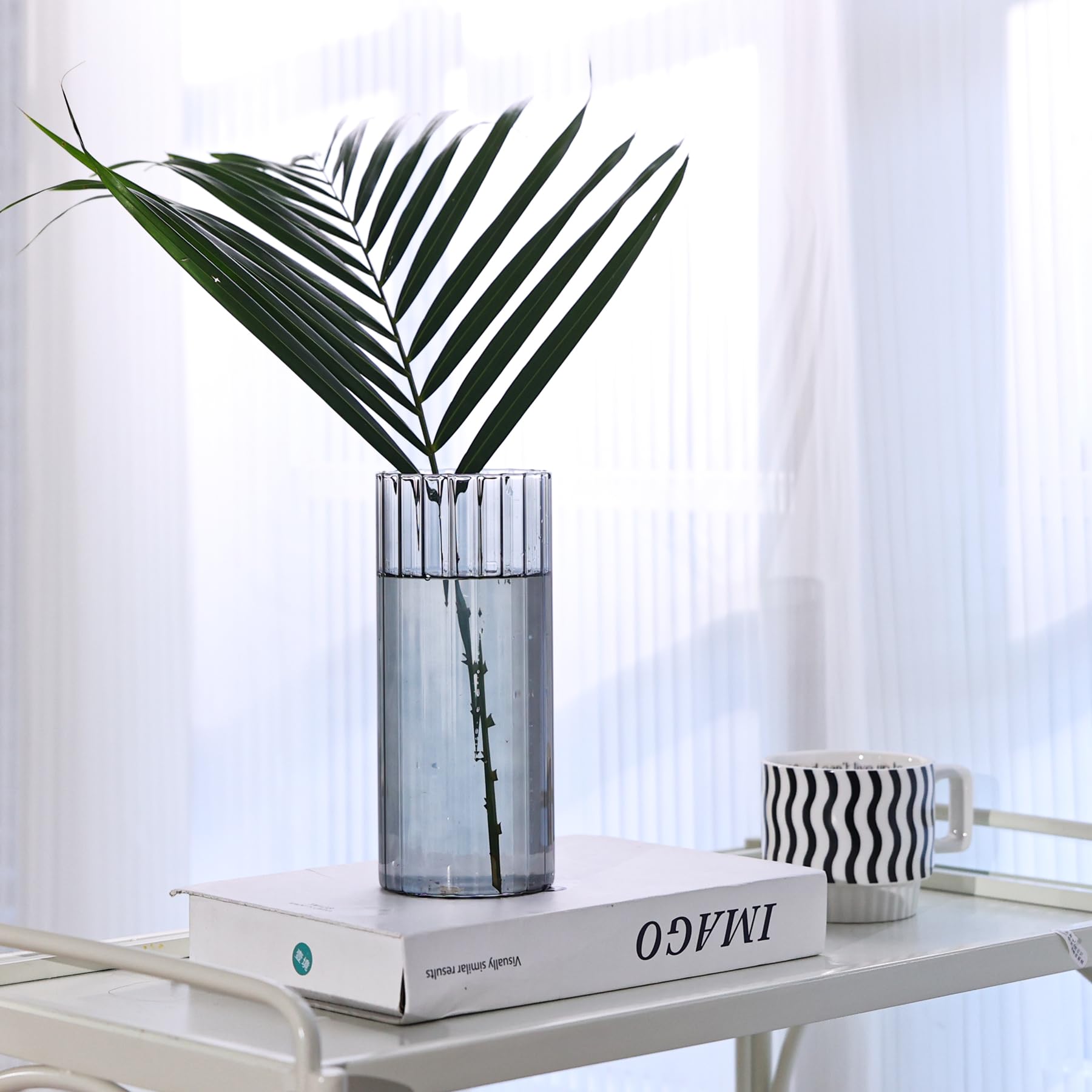 Decorative setup with a vase, book, and cup on a table against a white curtain background