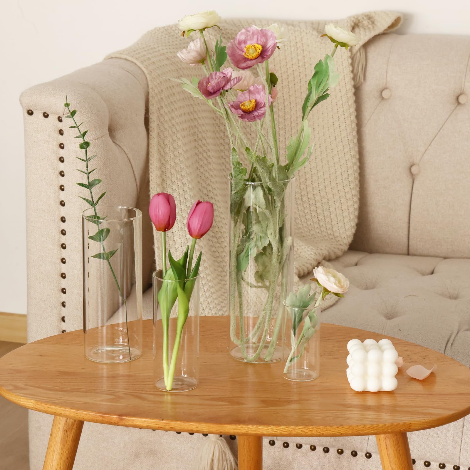 Decorative setup with pink tulips in clear vases on a wooden table in front of a beige sofa.