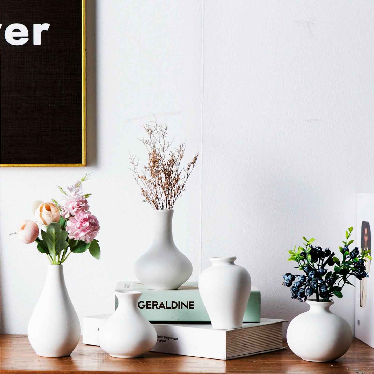Set of white vases with floral arrangements on a wooden surface against a white wall.