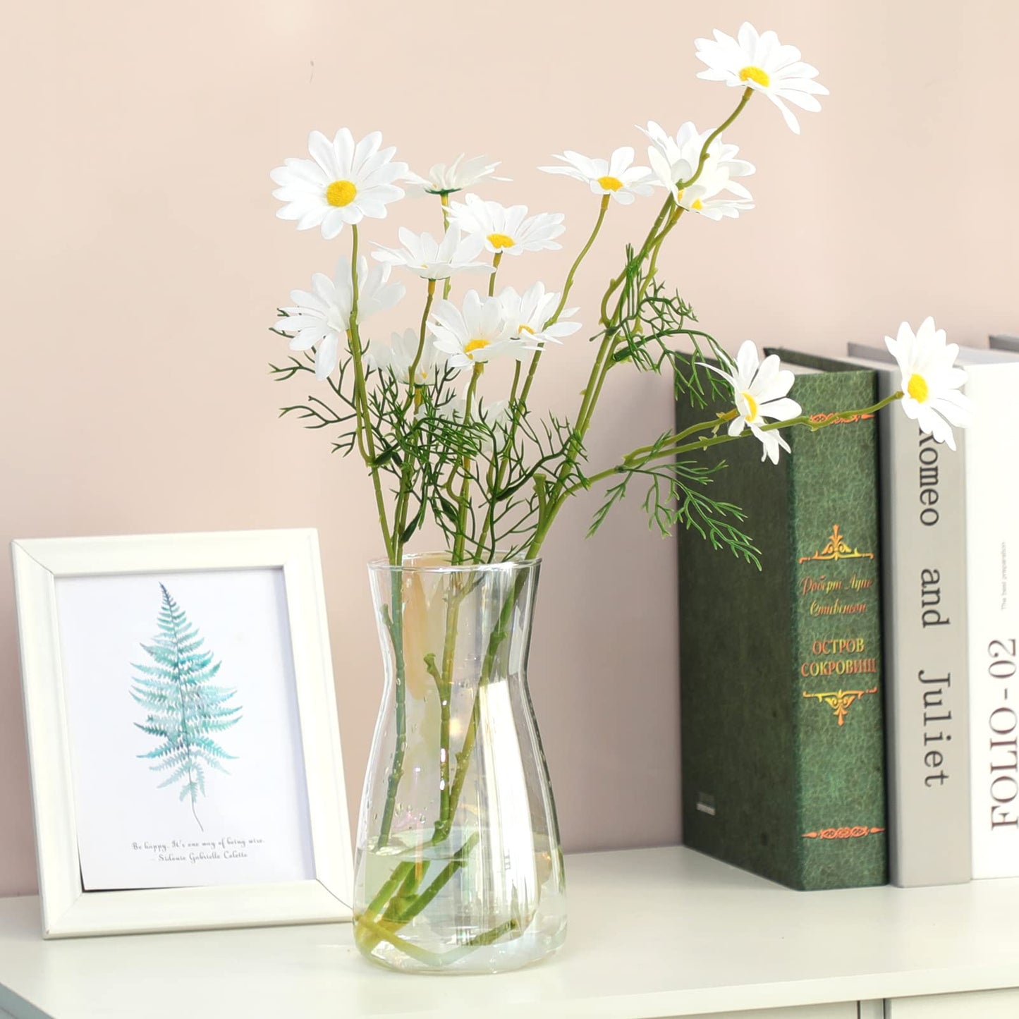 Clear vase with white flowers on a shelf with books and a framed picture.