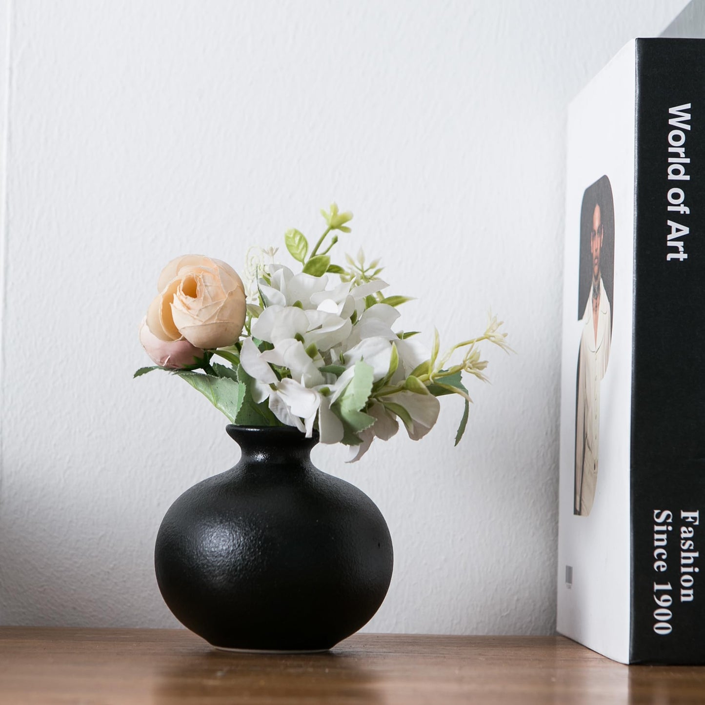 Black vase with flowers next to a book titled 'World of Art' on a wooden surface.