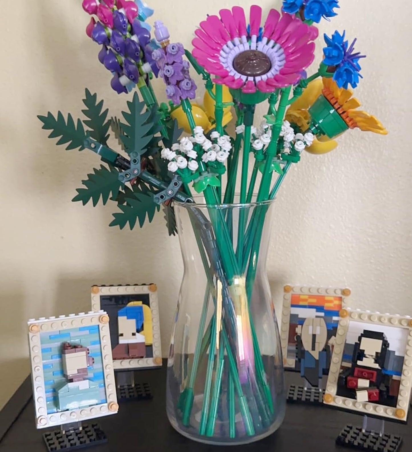 Vase with colorful LEGO flowers on a surface with small LEGO portraits.