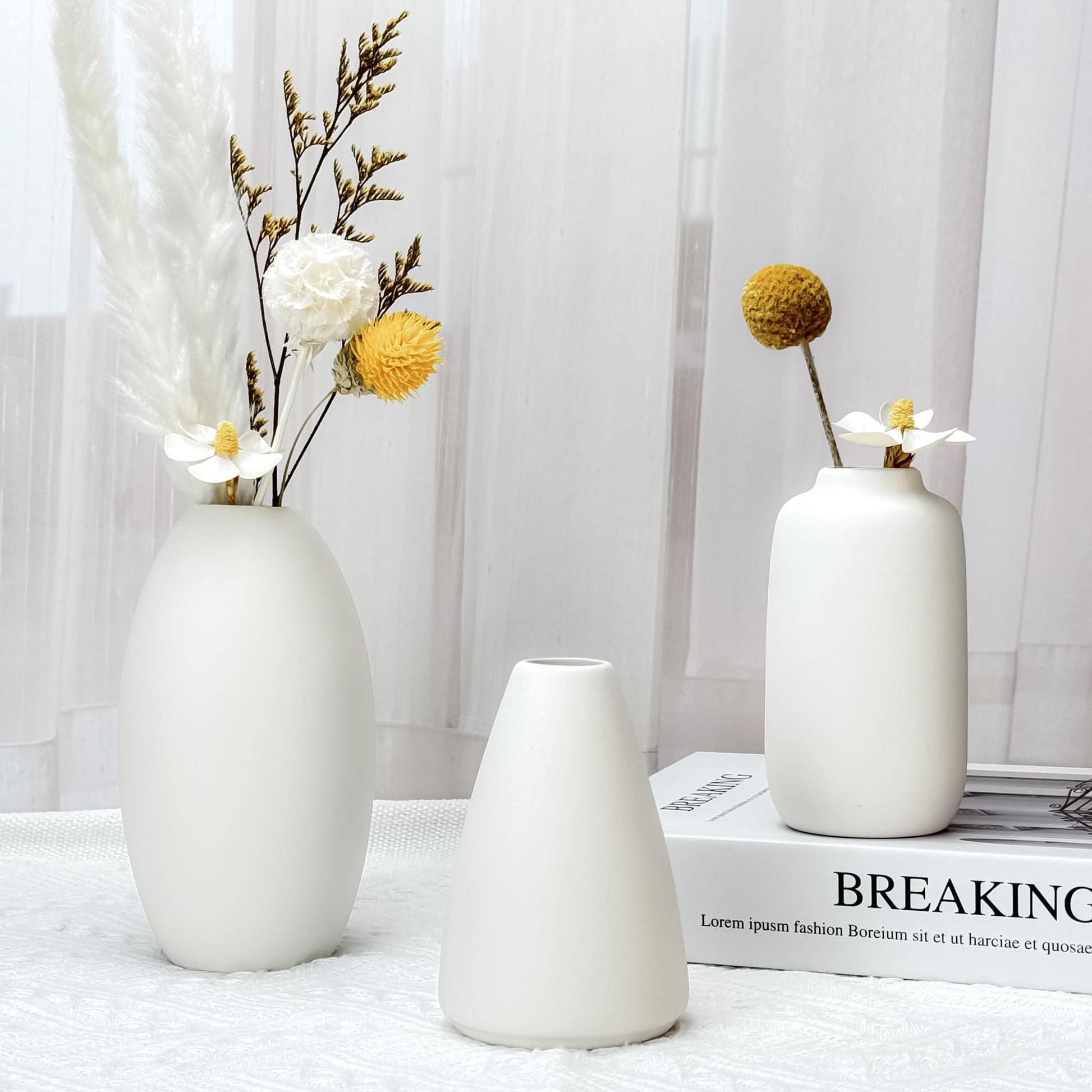 Three white vases with dried flowers on a light surface with a blurred background