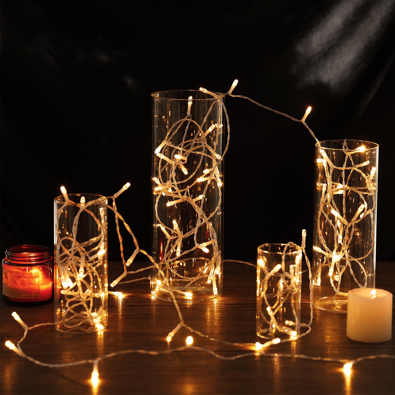 Decorative glass vases with string lights and candles on a dark background