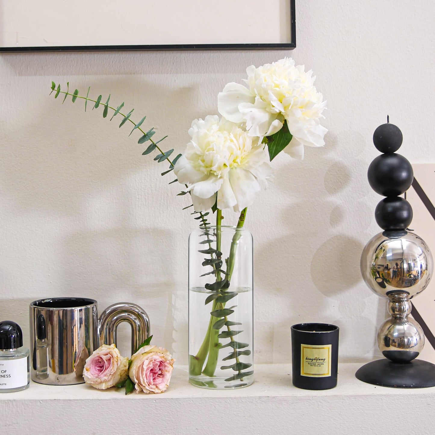 Decorative items including a vase with white flowers, candles, and a black and silver lamp on a shelf.