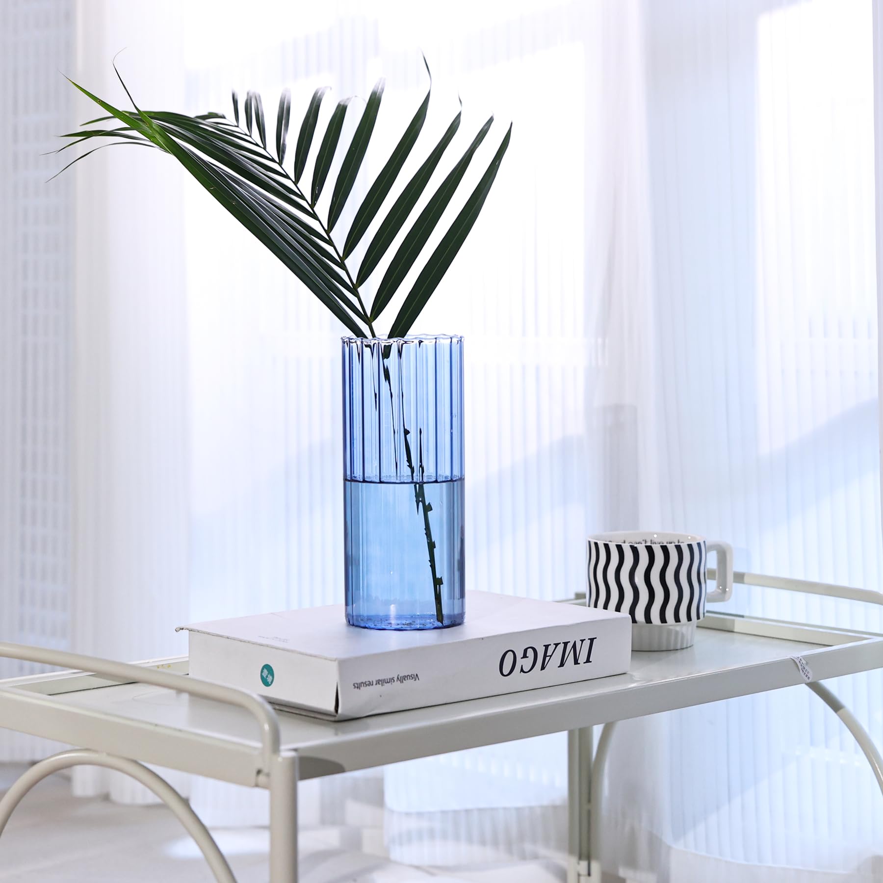 Blue vase with green leaves on a white table against a white curtain background