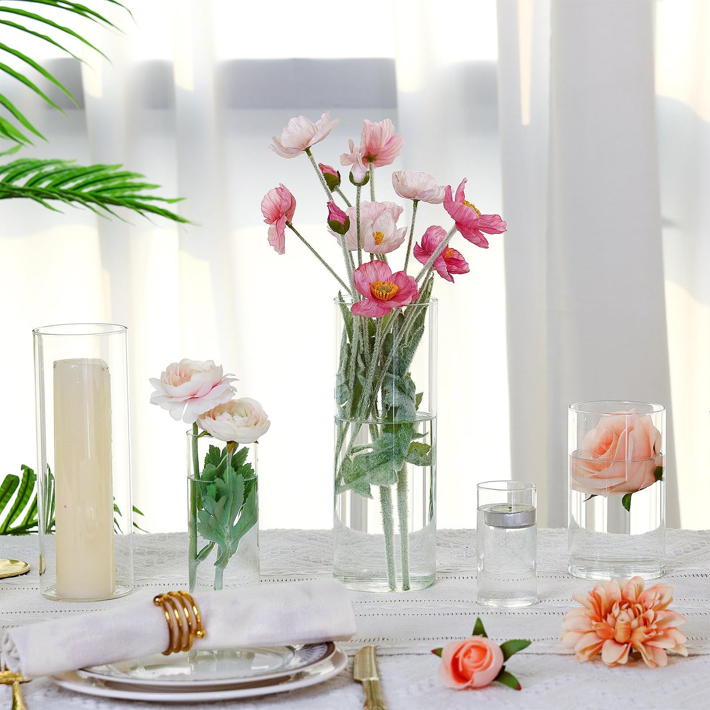 Table setting with pink flowers, candles, and greenery on a white tablecloth.