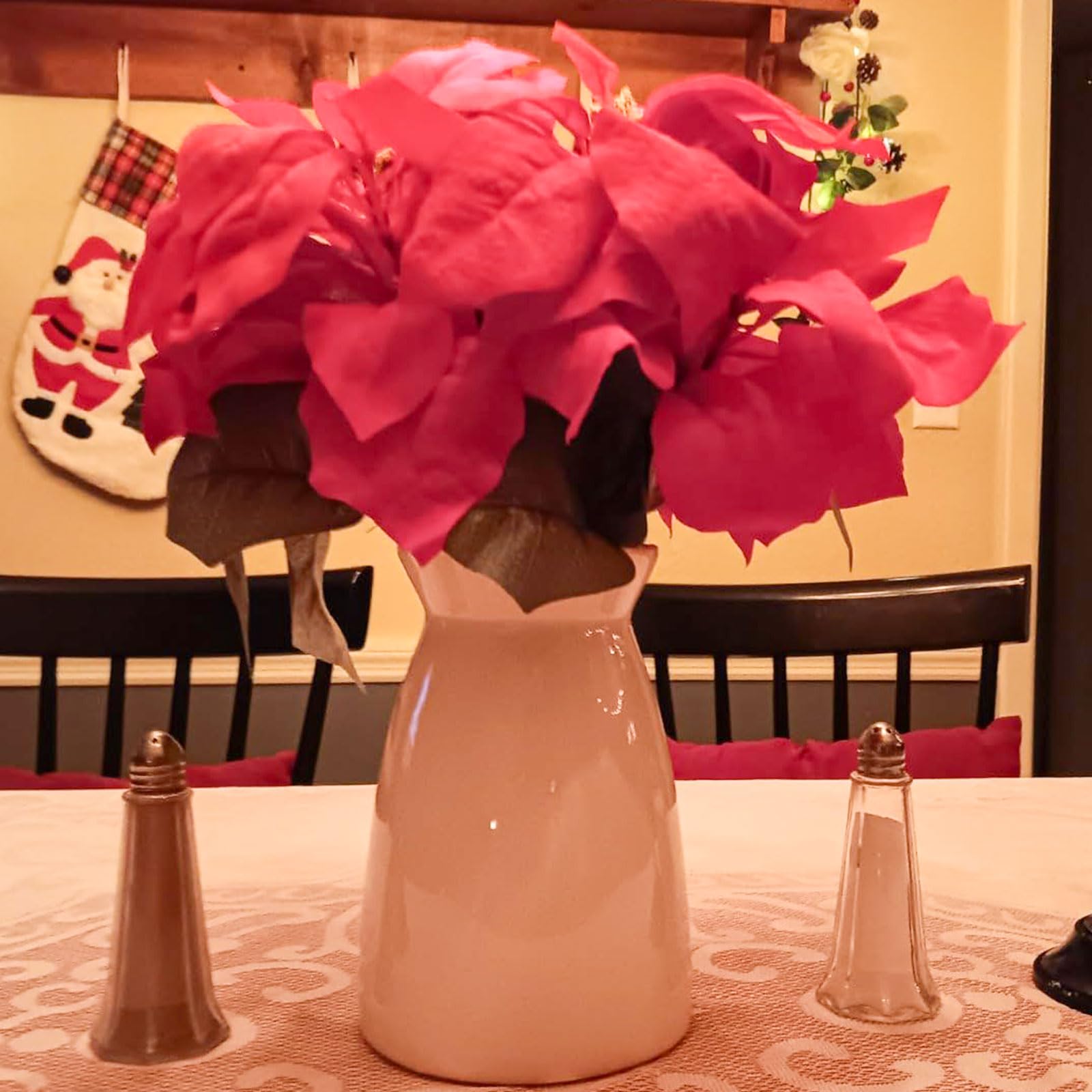 Pink poinsettias in a beige vase on a table with a Christmas stocking in the background.