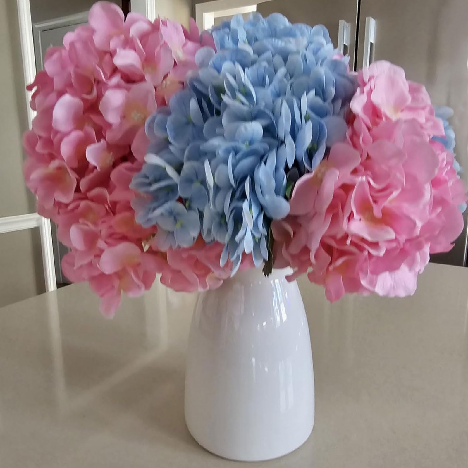 Bouquet of pink and blue flowers in a white vase on a table.