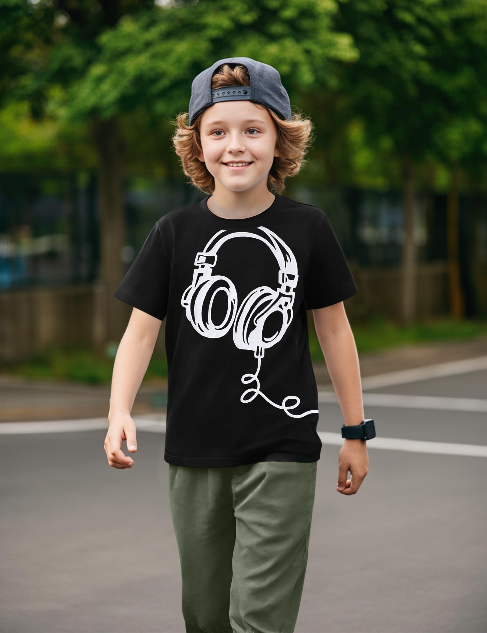 Child wearing a black t-shirt with headphones graphic and a cap, standing outdoors.
